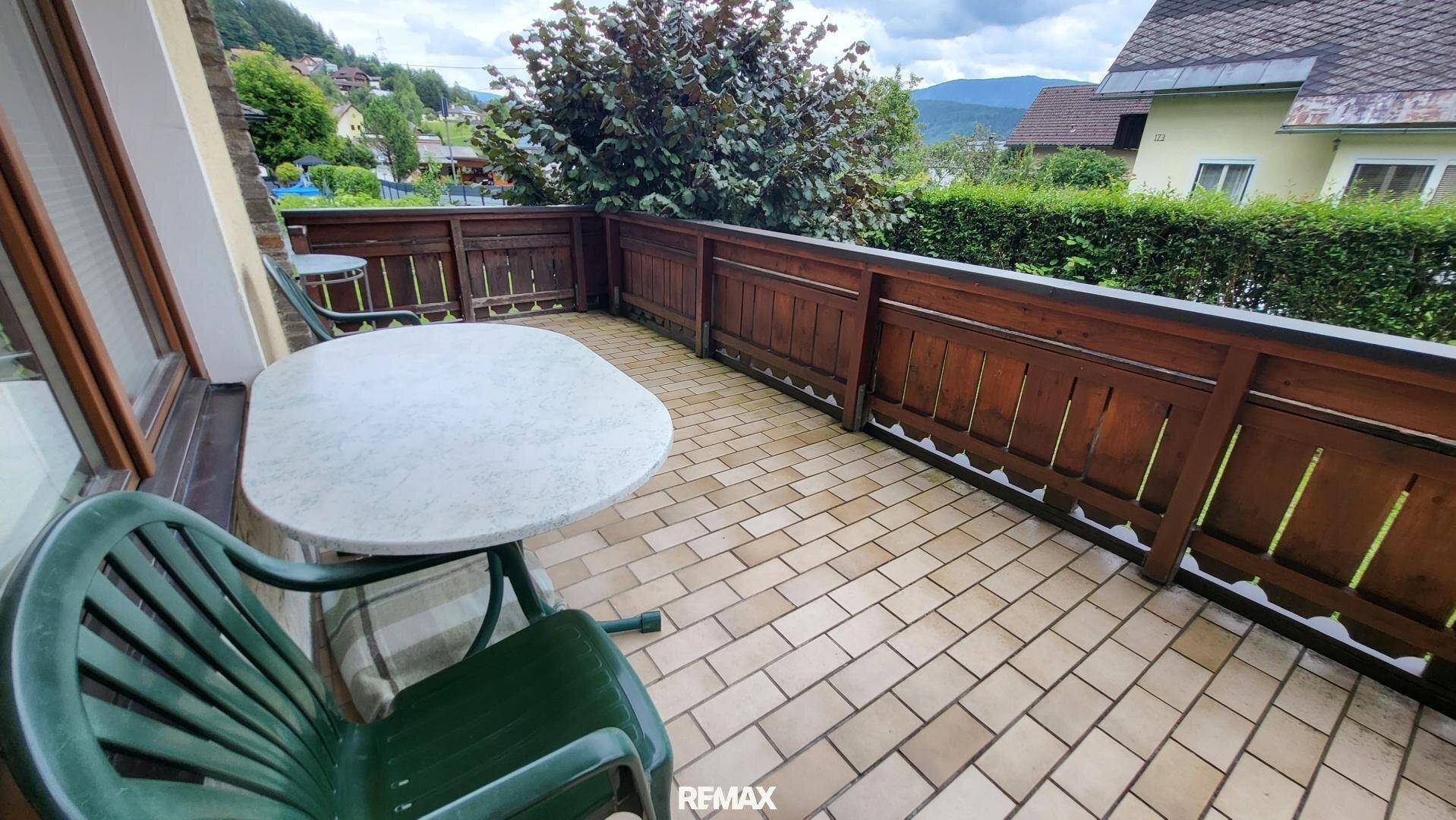 Balkon mit Fliesenboden, Holzbalkonbrüstung und Sitzgelegenheiten mit Blick auf die grüne Umgebung.