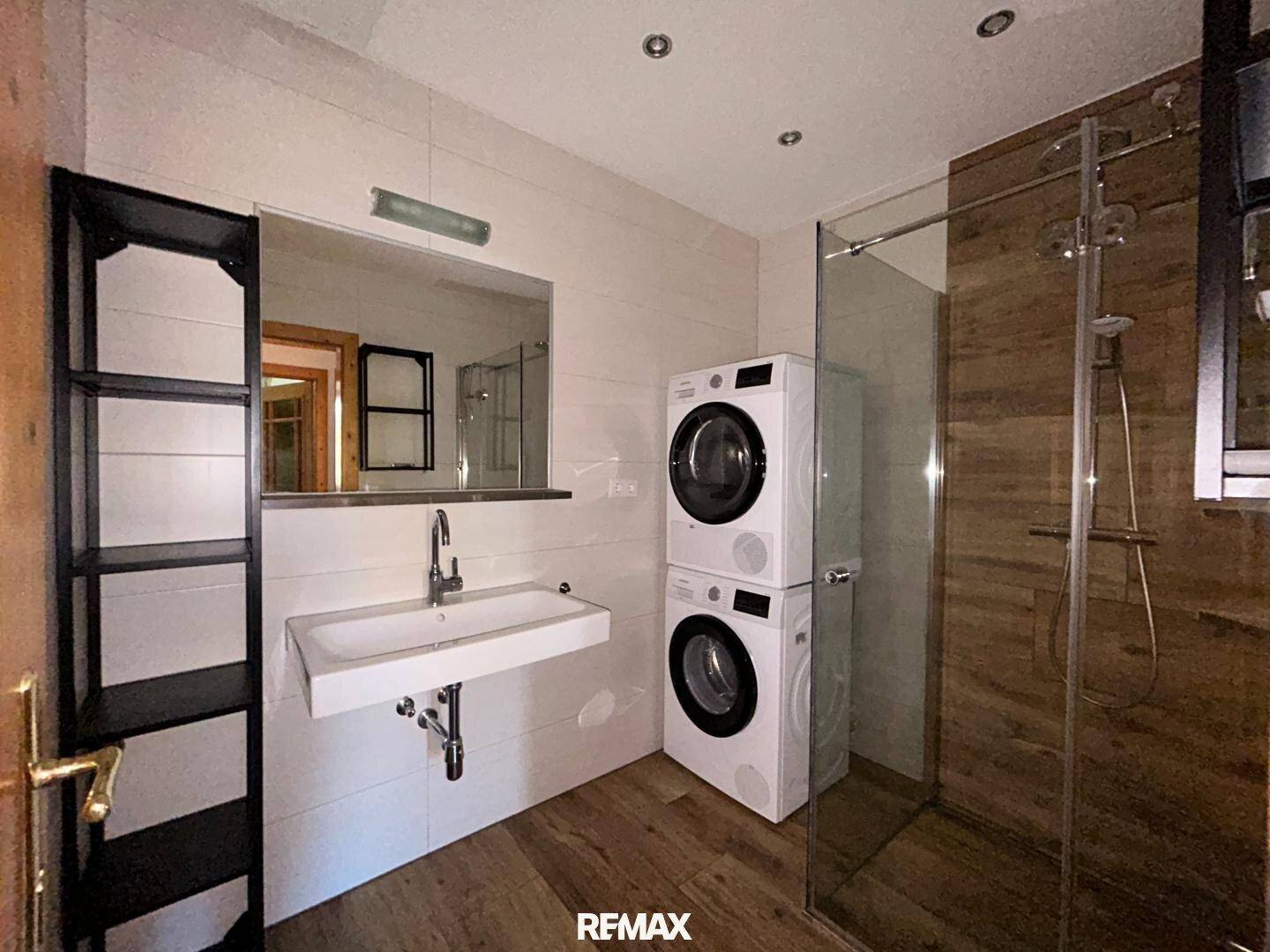 Modernes Badezimmer mit Dusche, Waschbecken und integrierter Waschmaschine und Trockner.