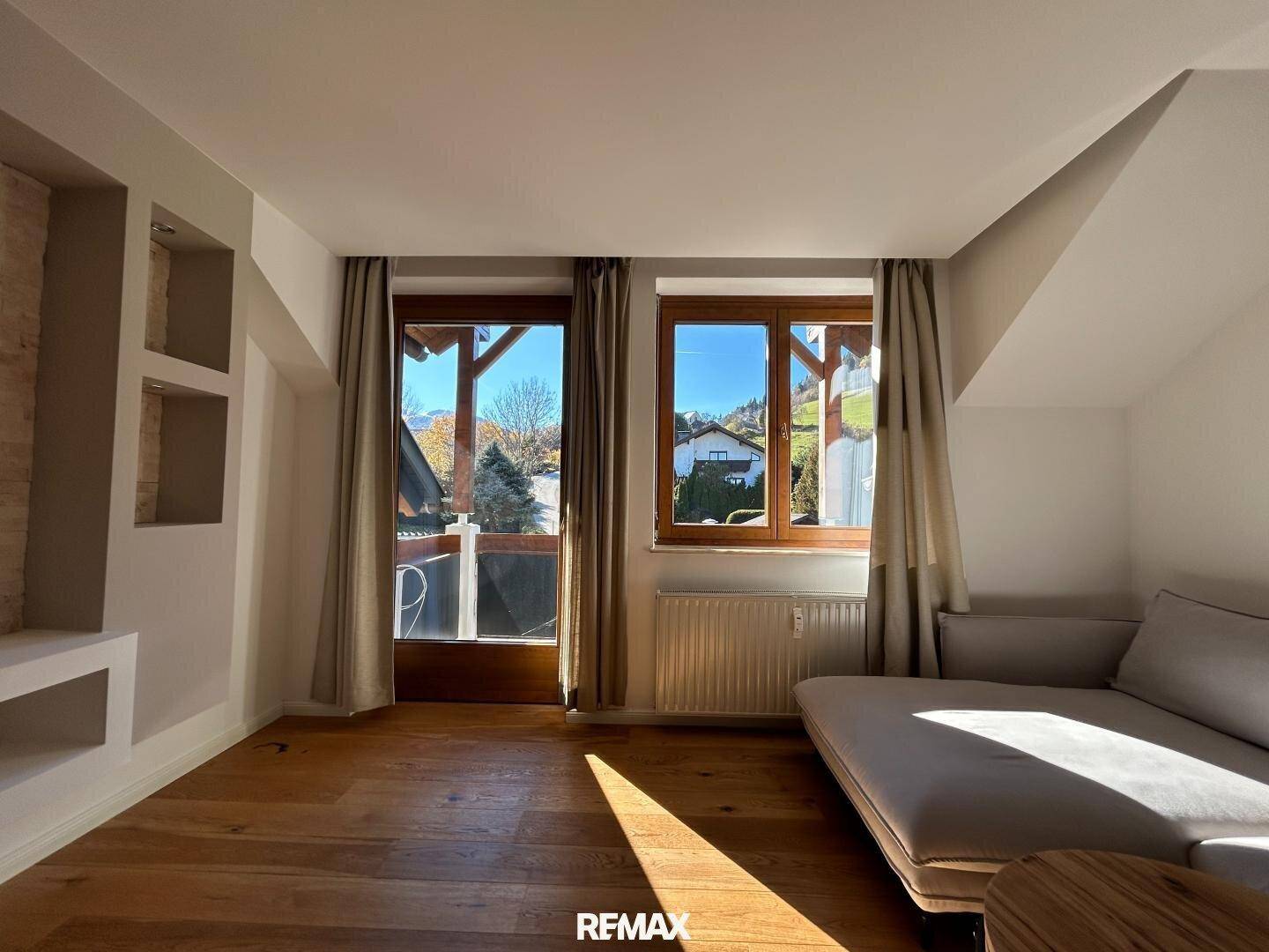 Lichtdurchflutetes Wohnzimmer mit Holzboden, schrägen Decken und Blick ins Grüne.