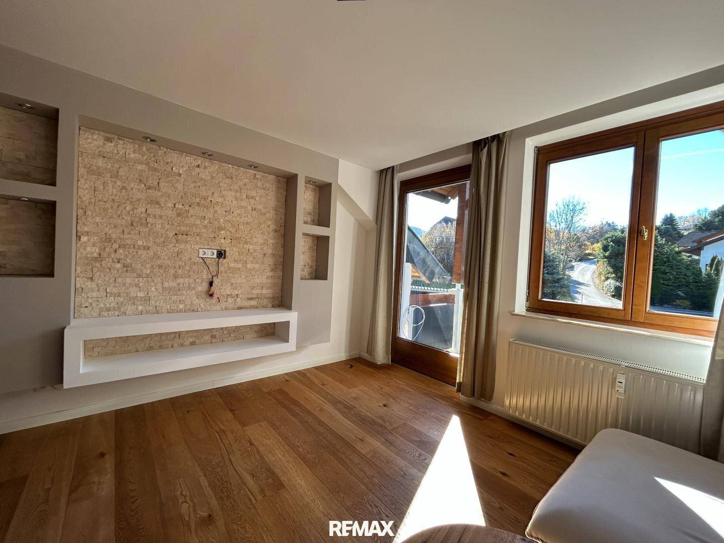 Geräumiges Wohnzimmer mit Holzboden, dekorativer Steinwand und viel Tageslicht.