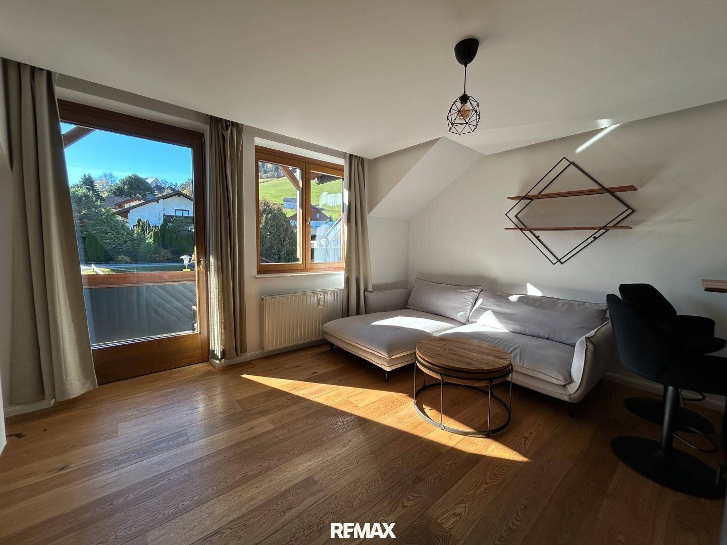Helles Wohnzimmer mit Holzboden, gemütlichem Sofa und Zugang zum Balkon mit Bergblick.