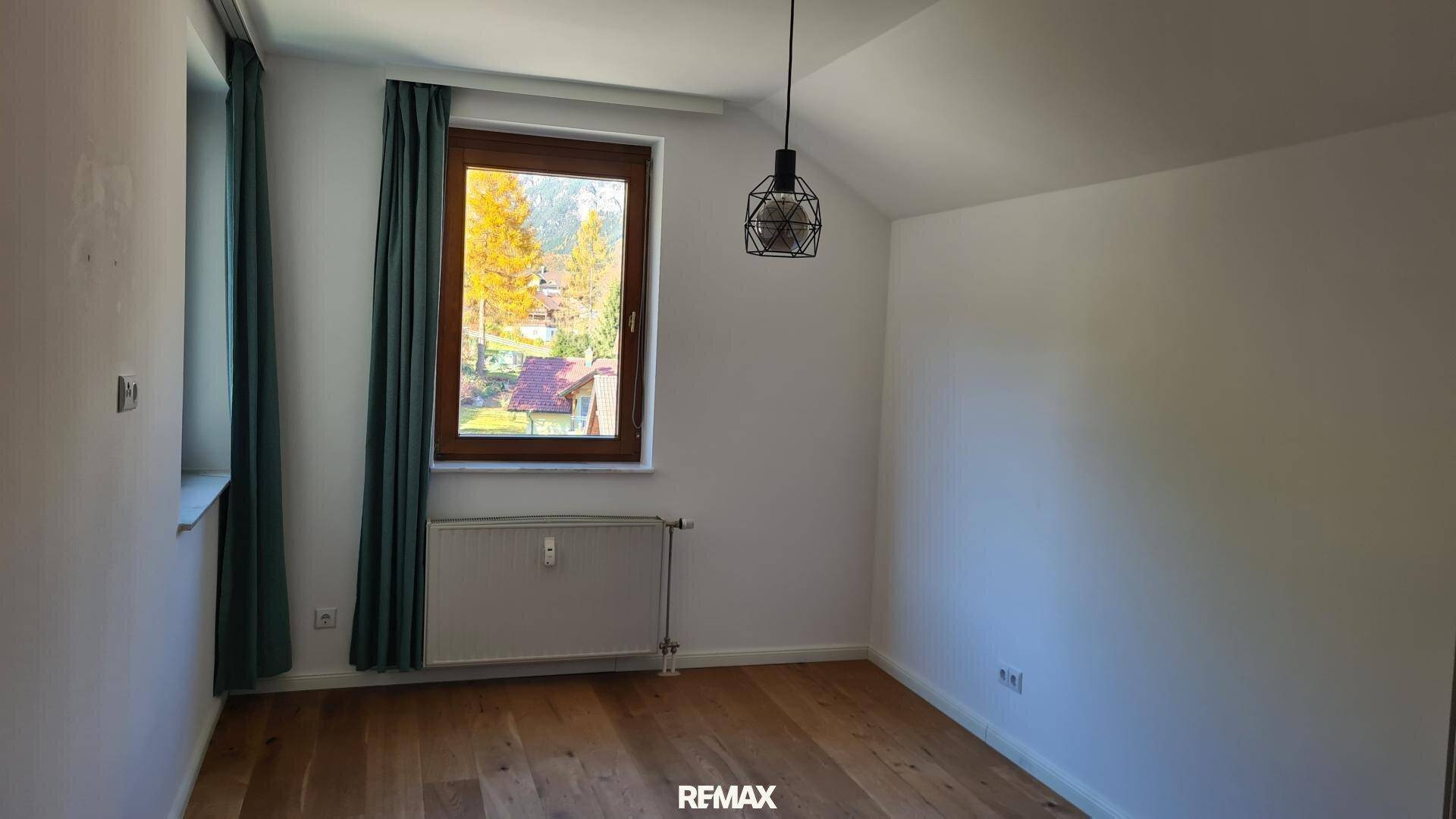Helles Schlafzimmer mit Holzboden, großem Fenster und Blick ins Grüne.