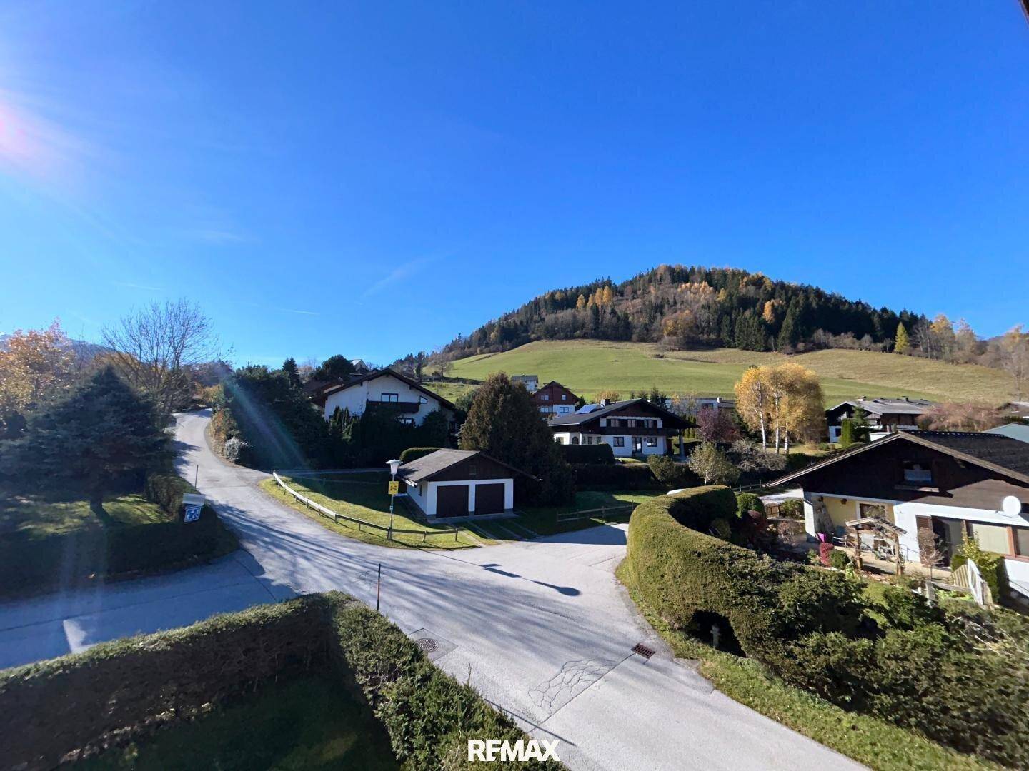 Weitläufiger Blick über die grüne Wohngegend mit Häusern und Hügeln unter strahlend blauem Himmel.