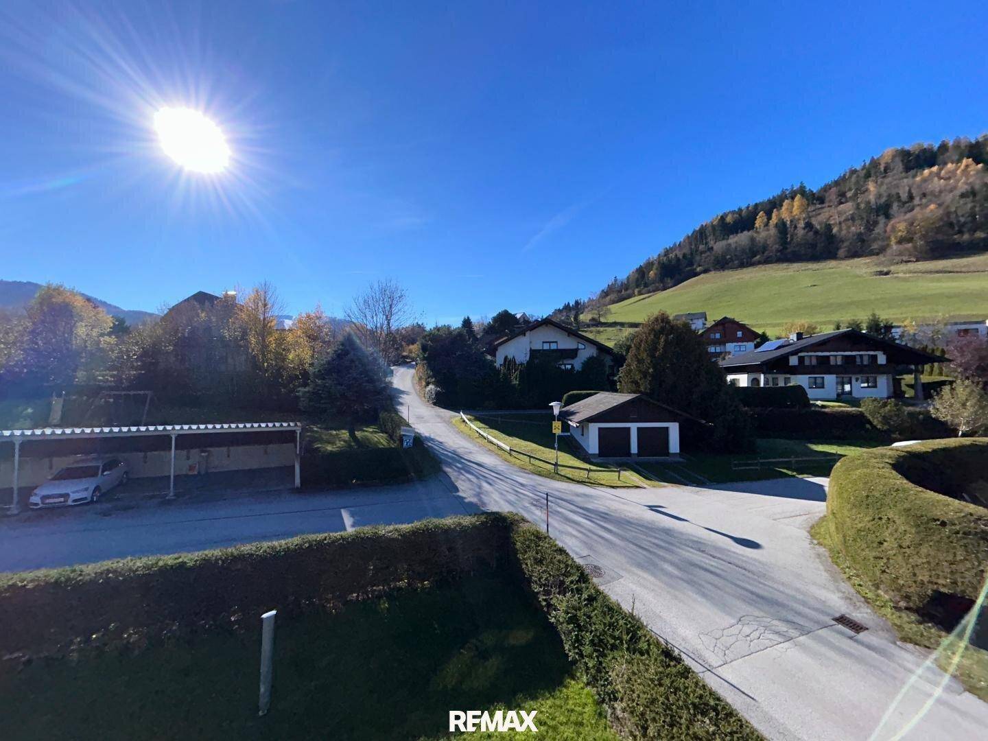 Panoramablick auf die sonnige Wohngegend mit Häusern, Gärten und grünen Hügeln.