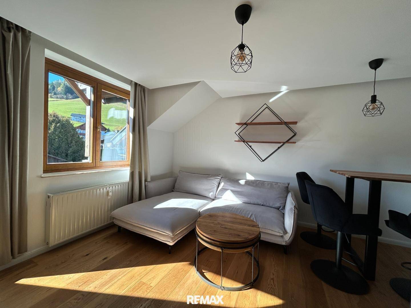 Heller Wohnbereich mit Holzboden, Sofa und Blick auf die grüne Umgebung.