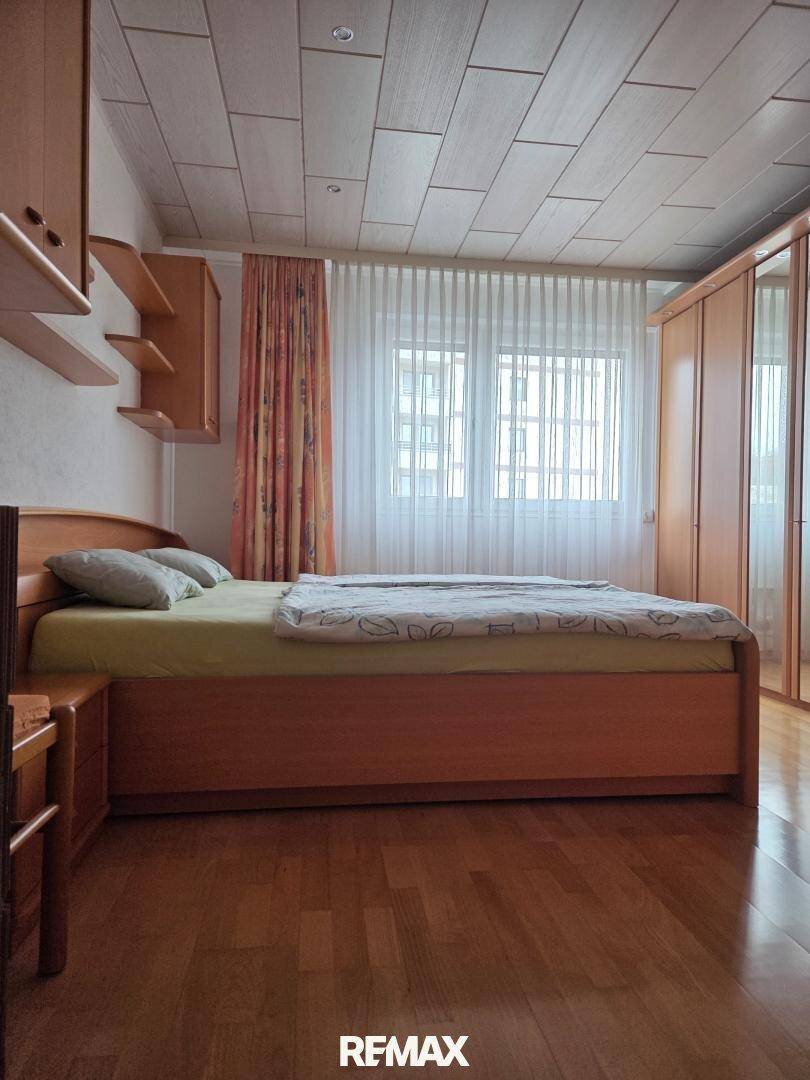 Helles Schlafzimmer mit Holzbett, Kleiderschränken und großen Fenstern.