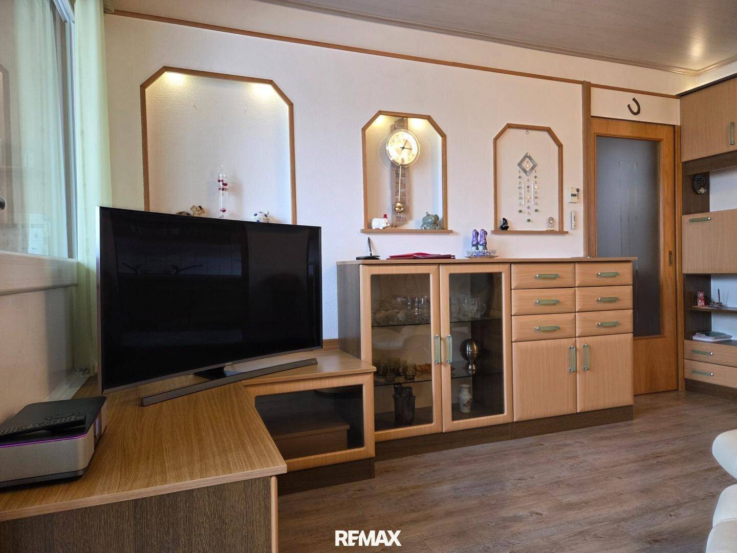 Gemütliches Wohnzimmer mit Holzmöbeln, Fernseher und dekorativen Wandnischen.