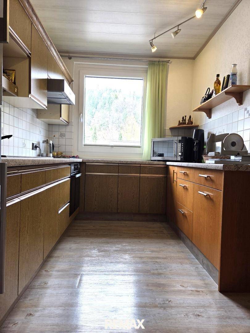 Funktionale Küche mit Holzschränken, weißen Fliesen und einem Fenster mit Blick ins Grüne.