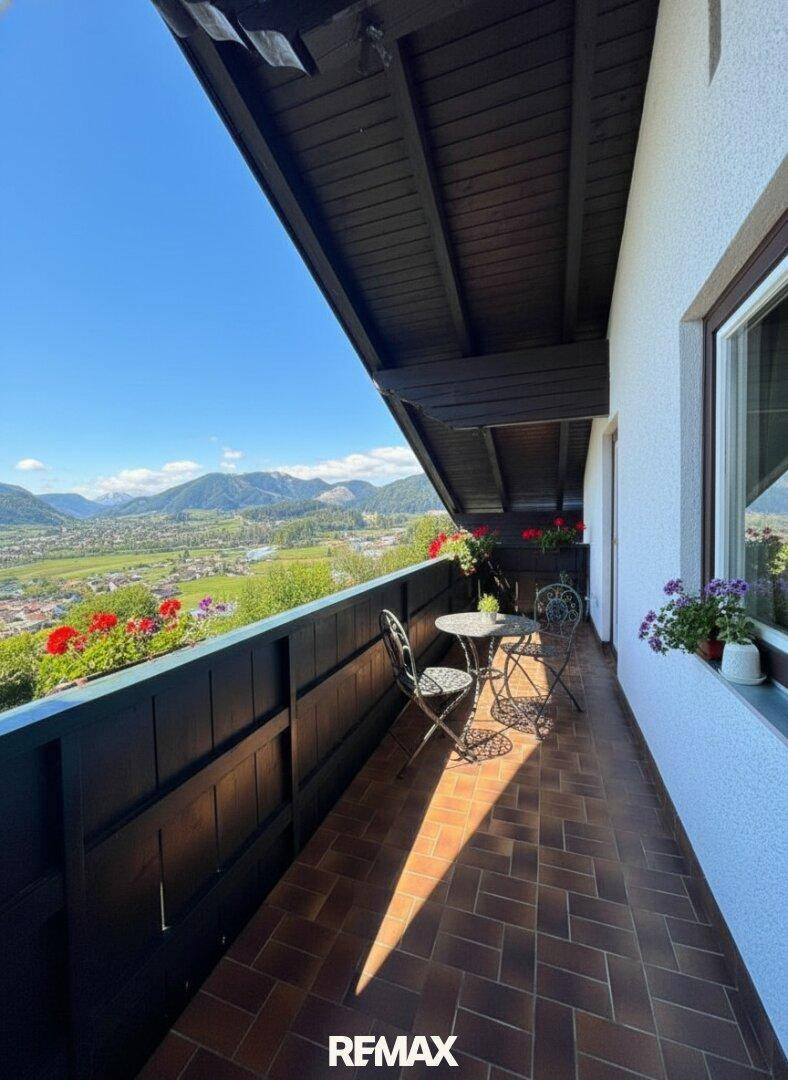 Sonniger Balkon mit Fliesenboden, Gartenmöbeln und weitem Blick über das Tal.