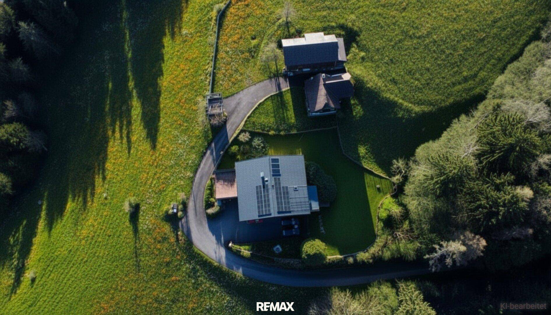 Luftaufnahme des Anwesens mit Haus, Zufahrt und weitläufiger grüner Umgebung.