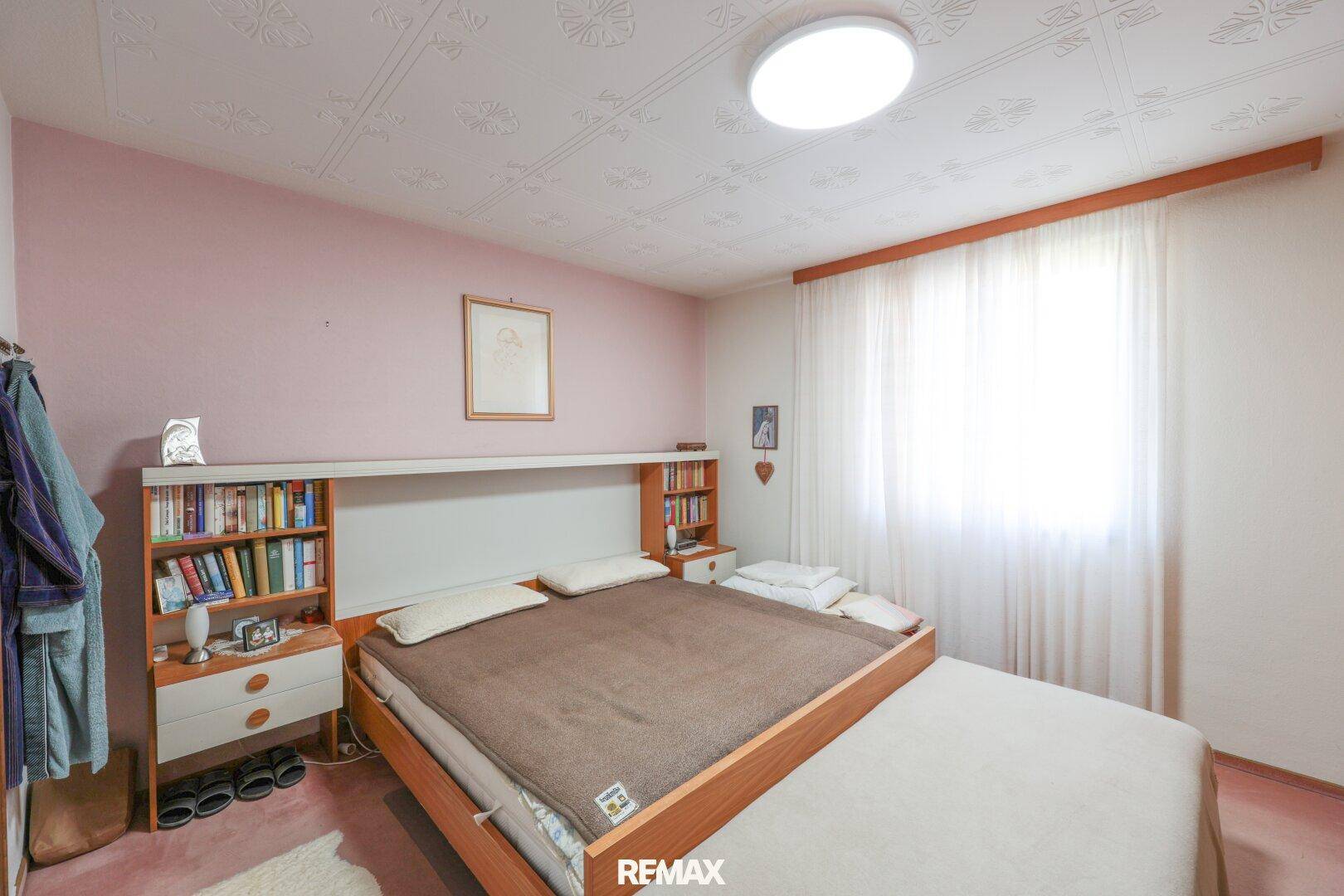 Helles Schlafzimmer mit Doppelbett, integriertem Bücherregal und rosa Wänden.