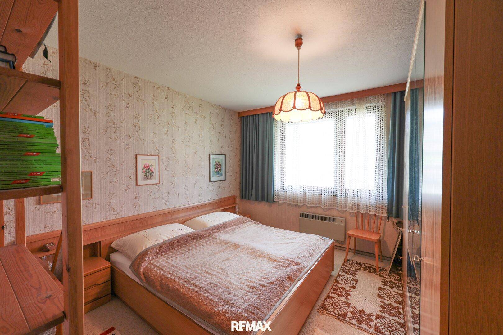 Gemütliches Schlafzimmer mit Doppelbett, Holzmöbeln und gemusterter Tapete.
