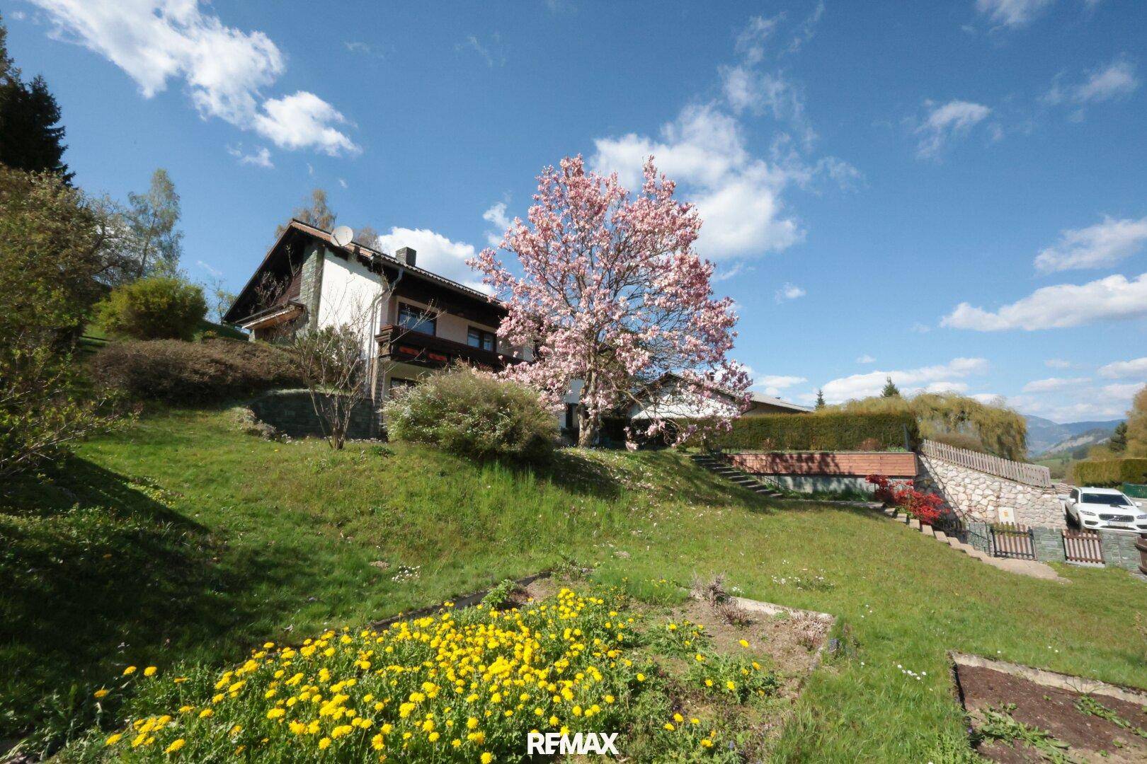 Haus mit großem Garten und blühenden Blumen in sonniger Hanglage.
