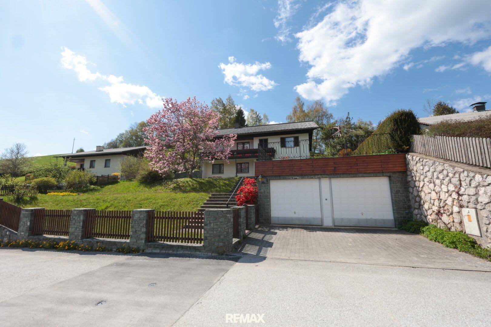 Hausansicht von der Straße mit Doppelgarage und blühendem Baum im Vorgarten.