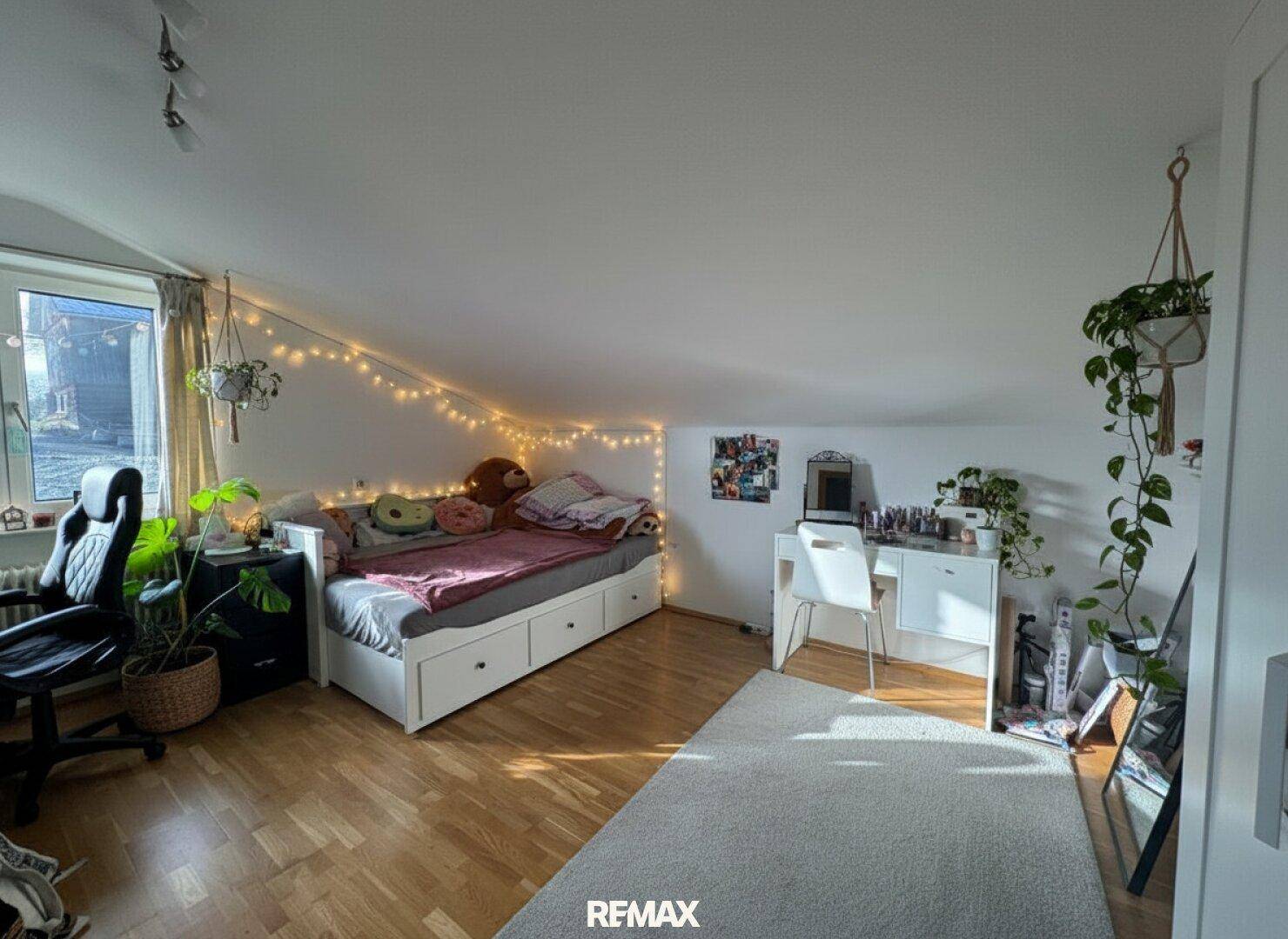 Helles Schlafzimmer mit Holzboden, Schreibtisch und gemütlicher Lichterkette.