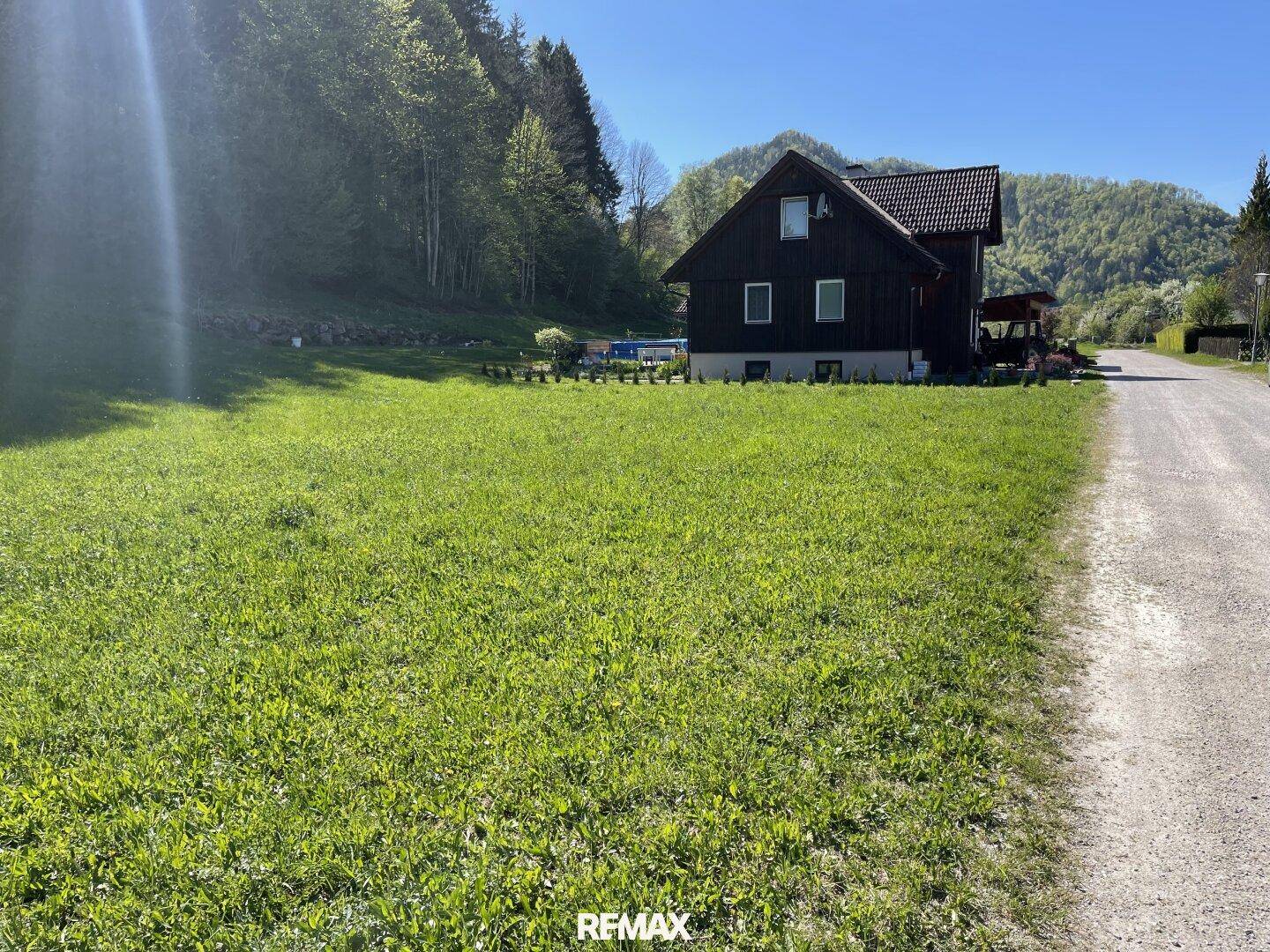 Geräumige Rasenfläche neben einem traditionellen Haus, umgeben von Wald und Bergen.