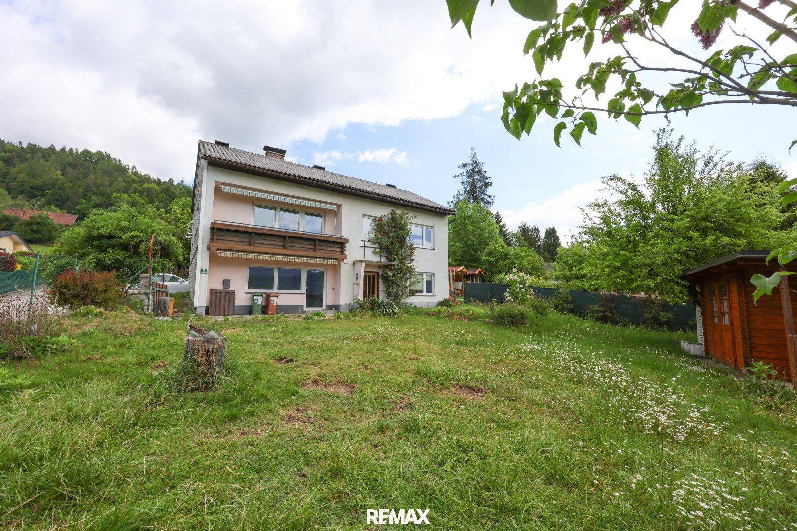 Das Haus von vorne mit großem Garten und einem kleinen Holzschuppen im Hintergrund.
