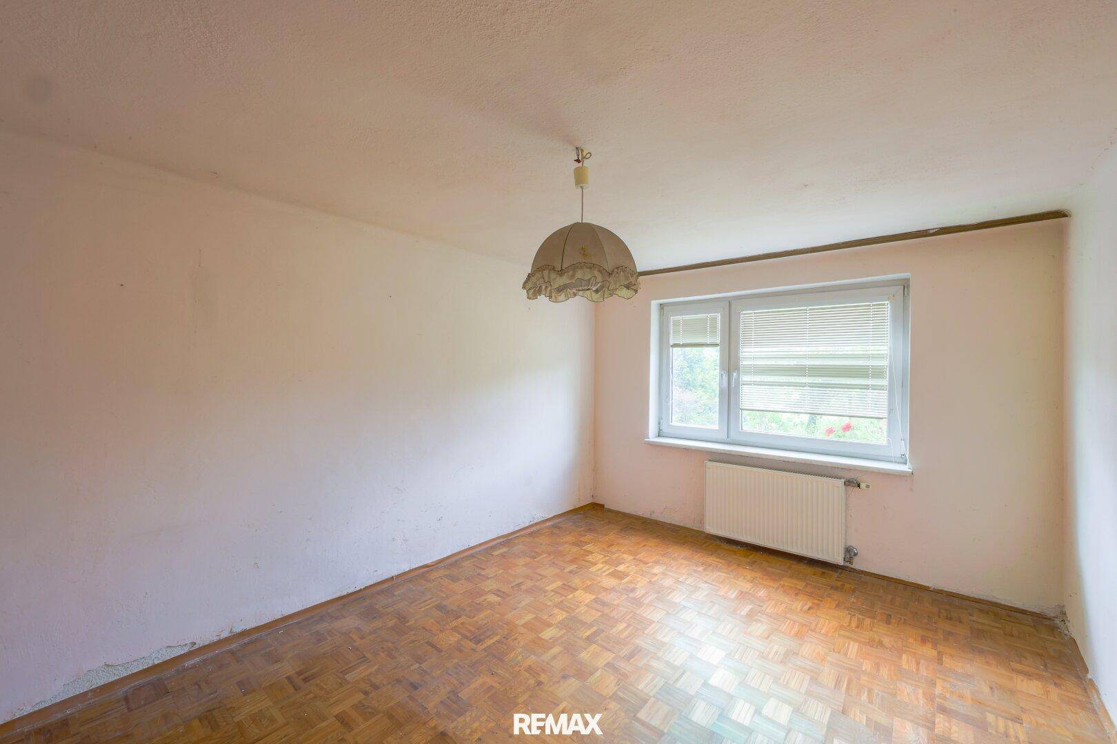 Helles Schlafzimmer mit Parkettboden und einem Fenster, das viel Tageslicht hereinlässt.