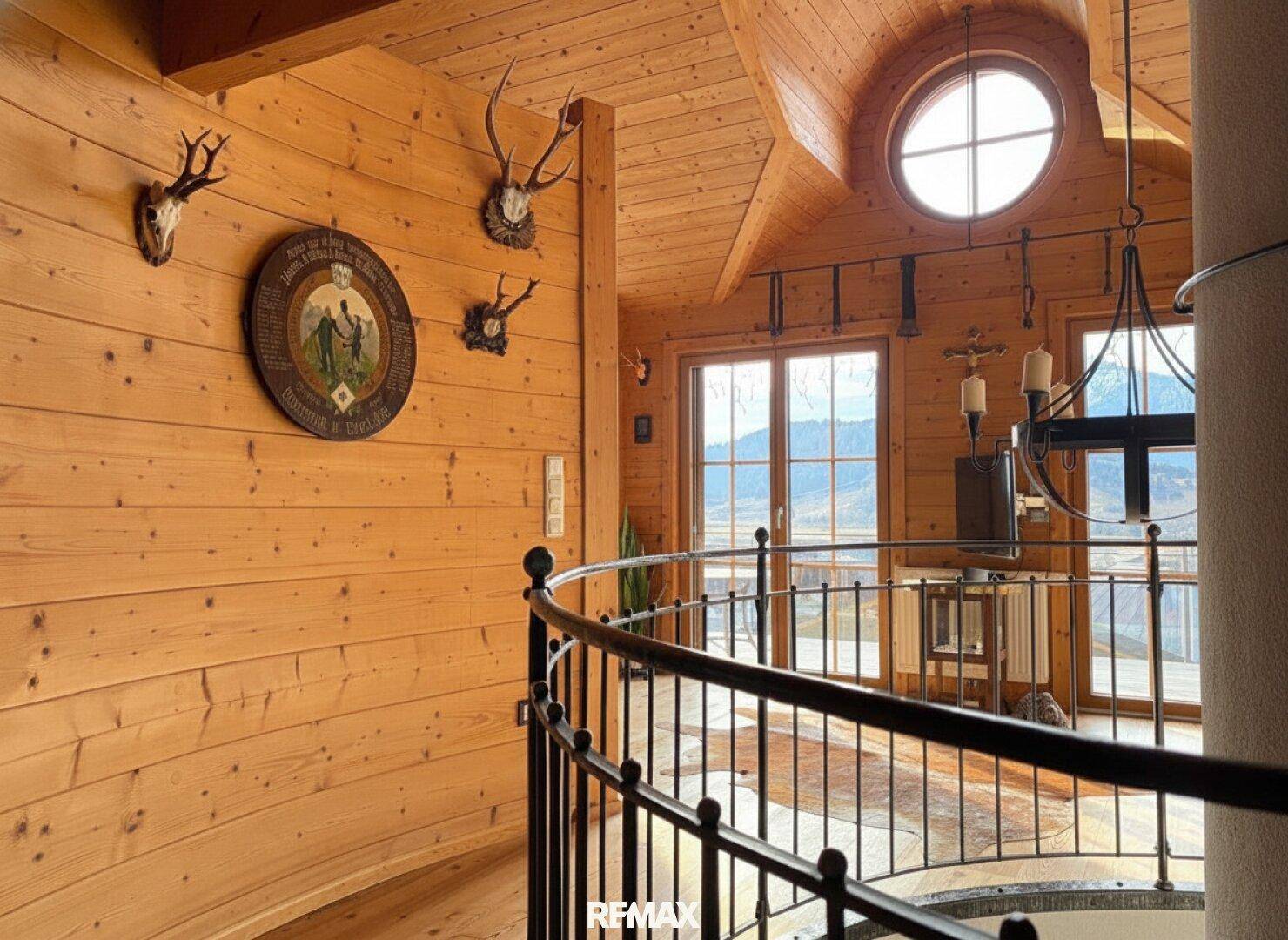 Galerie im Obergeschoss mit Holzwänden, Rundfenster und großen Fenstern, die einen weiten Bergblick bieten.