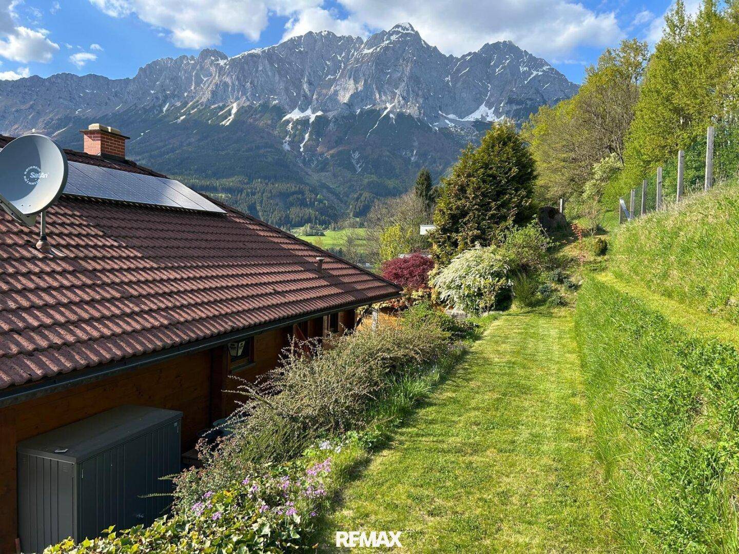 Seitenansicht des Hauses mit gepflegtem Rasen, Garten und einem beeindruckenden Bergblick im Hintergrund.