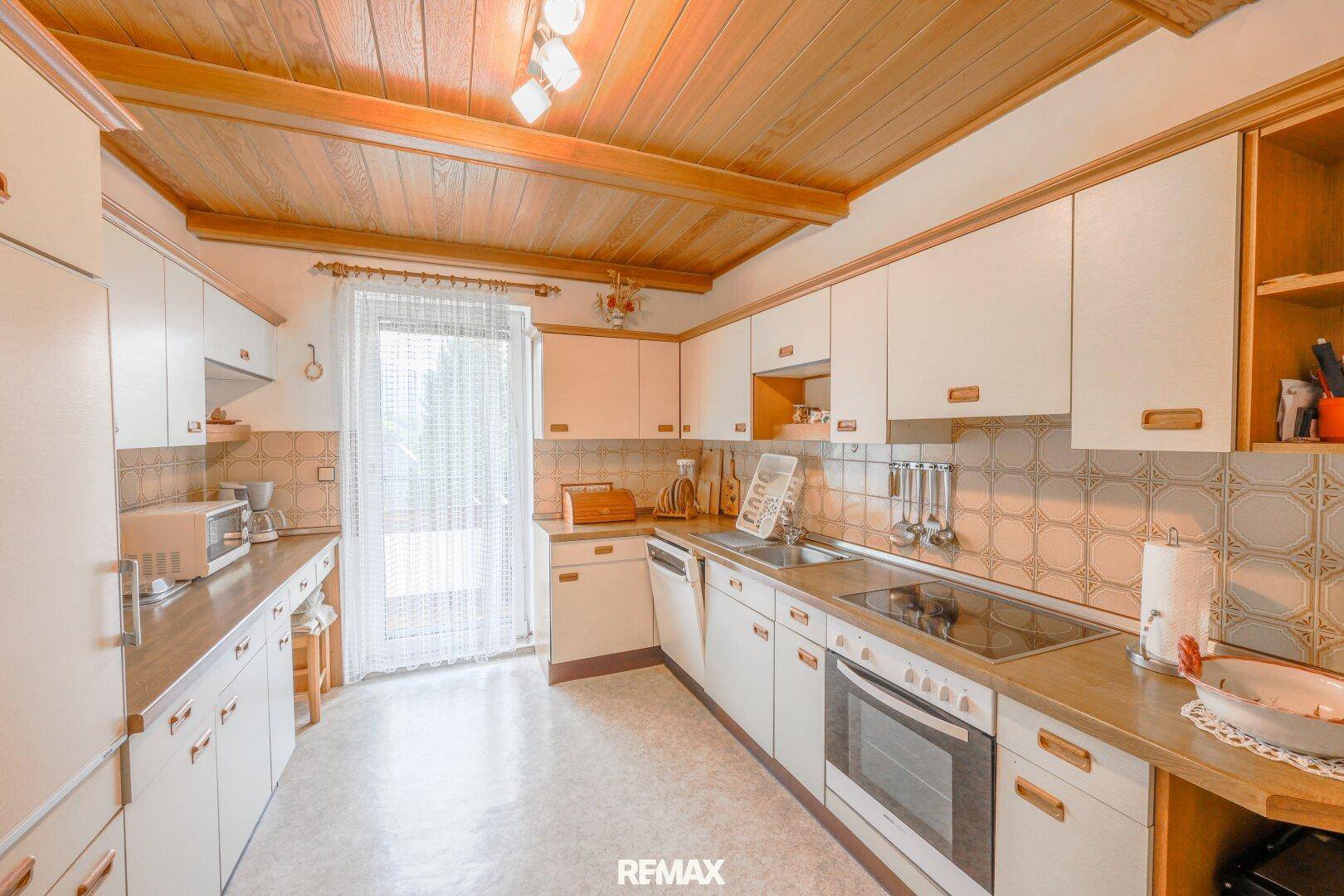 Funktionale Küche mit weißen Einbauschränken, Holzdecke und integrierten Geräten.