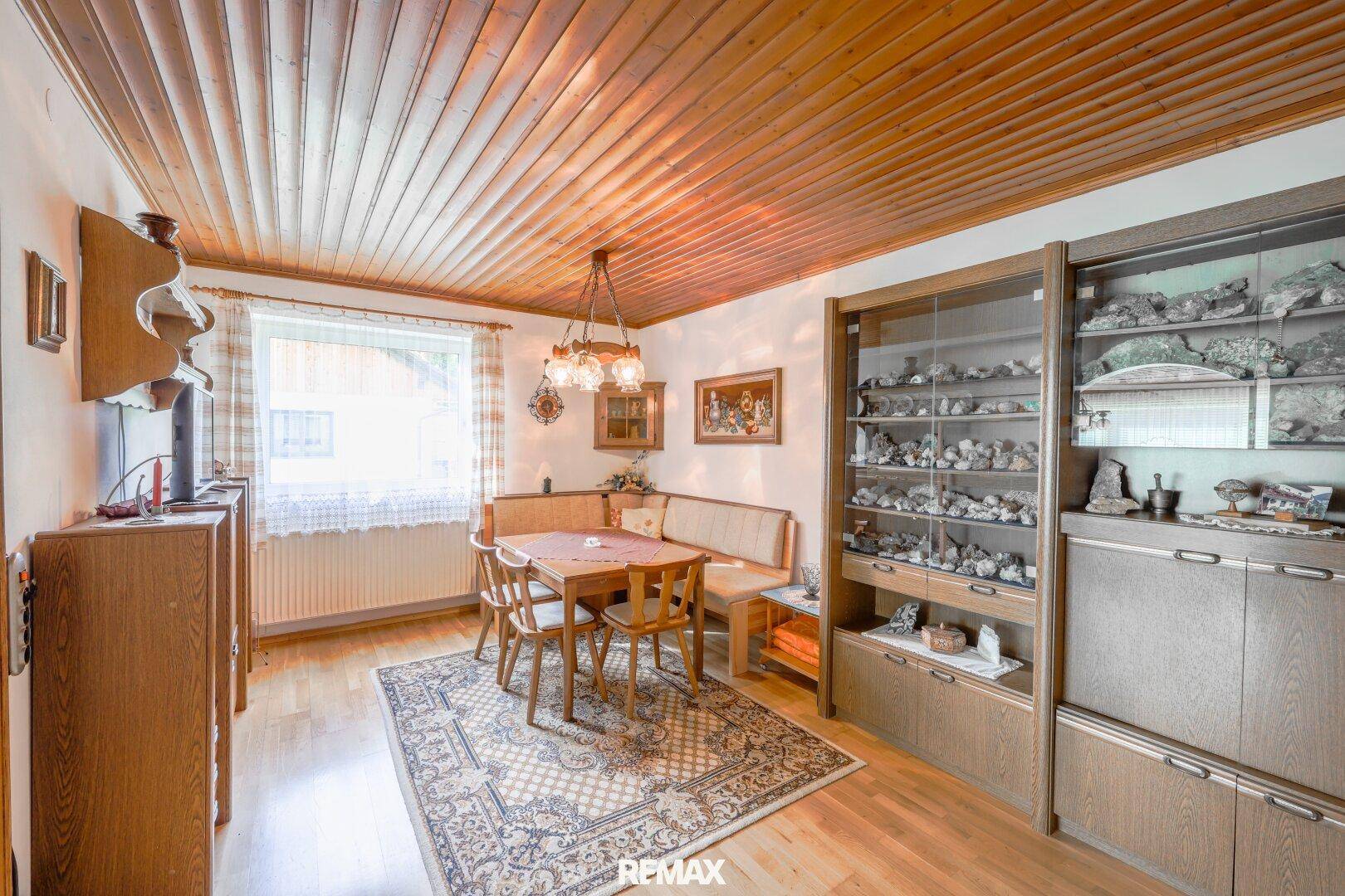 Essbereich mit Eckbank, Holztisch und einem großen Schrank mit Sammlerstücken.