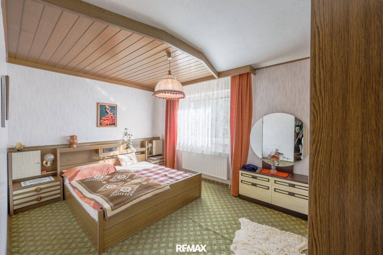 Schlafzimmer mit Doppelbett, grünem Teppichboden und traditioneller Holzdecke.