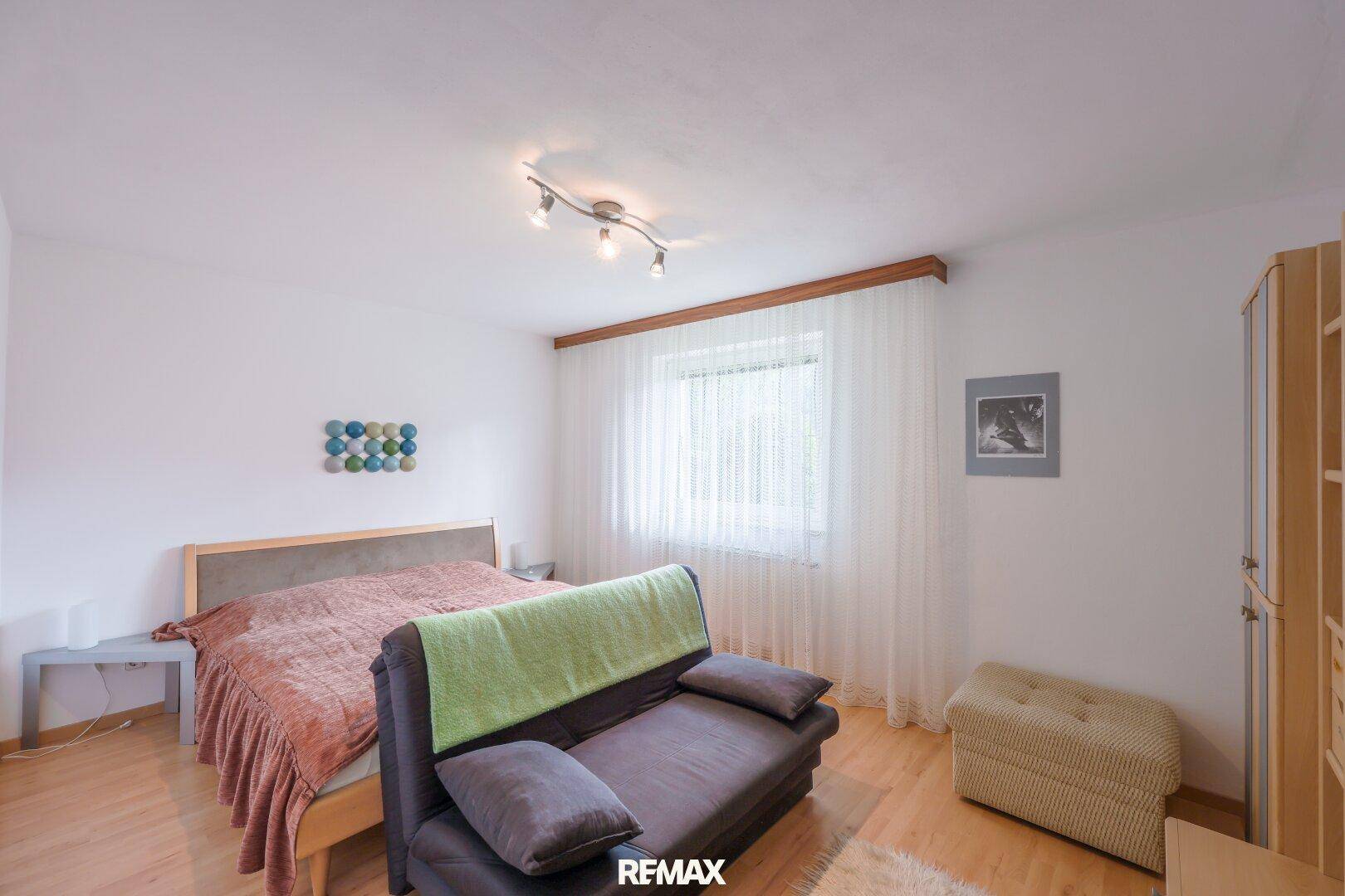 Helles Schlafzimmer mit Doppelbett, Schlafsofa und hellem Holzfußboden.