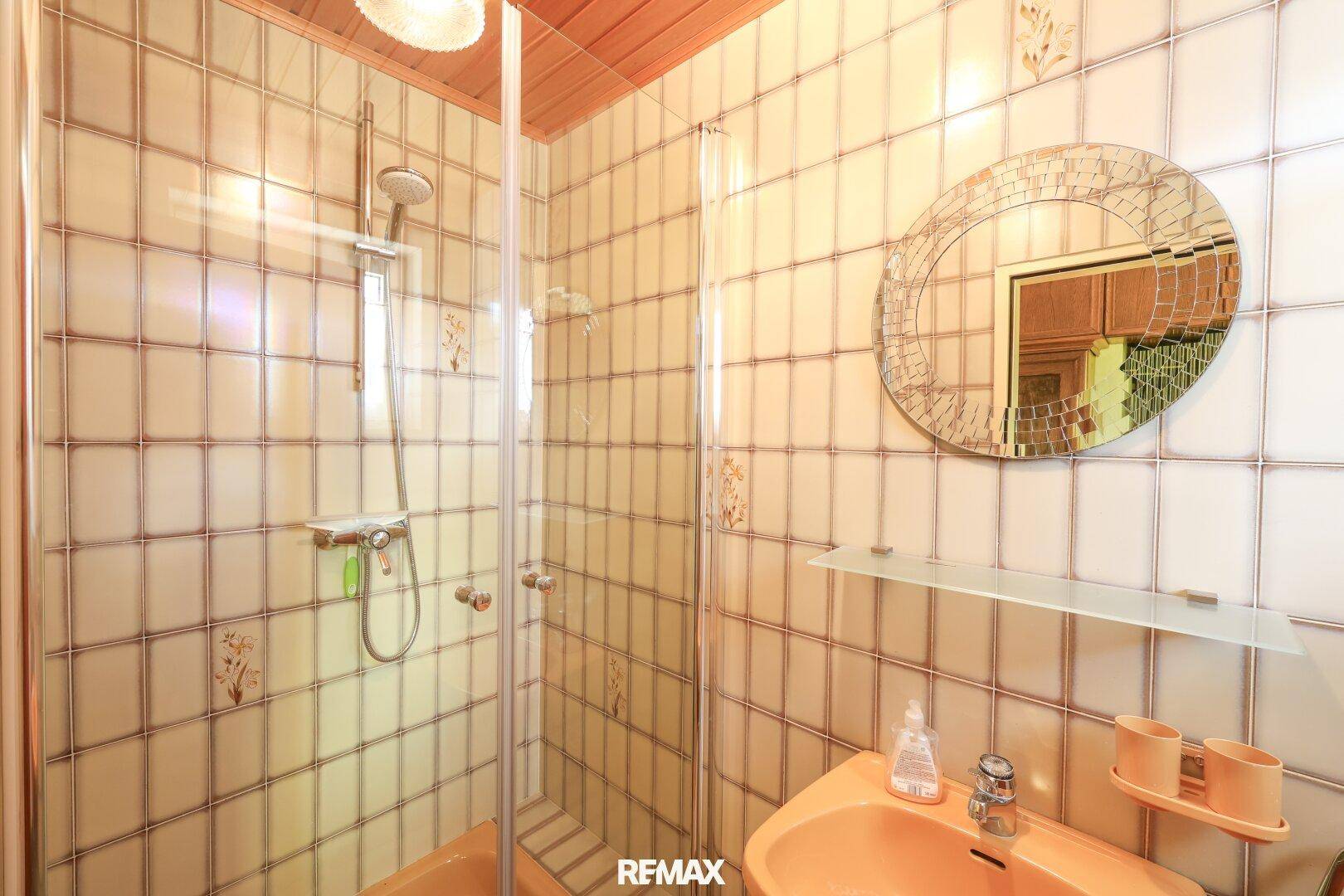 Badezimmer mit Duschkabine, orangefarbenem Waschbecken und Fliesen im Retro-Stil der 80er Jahre.
