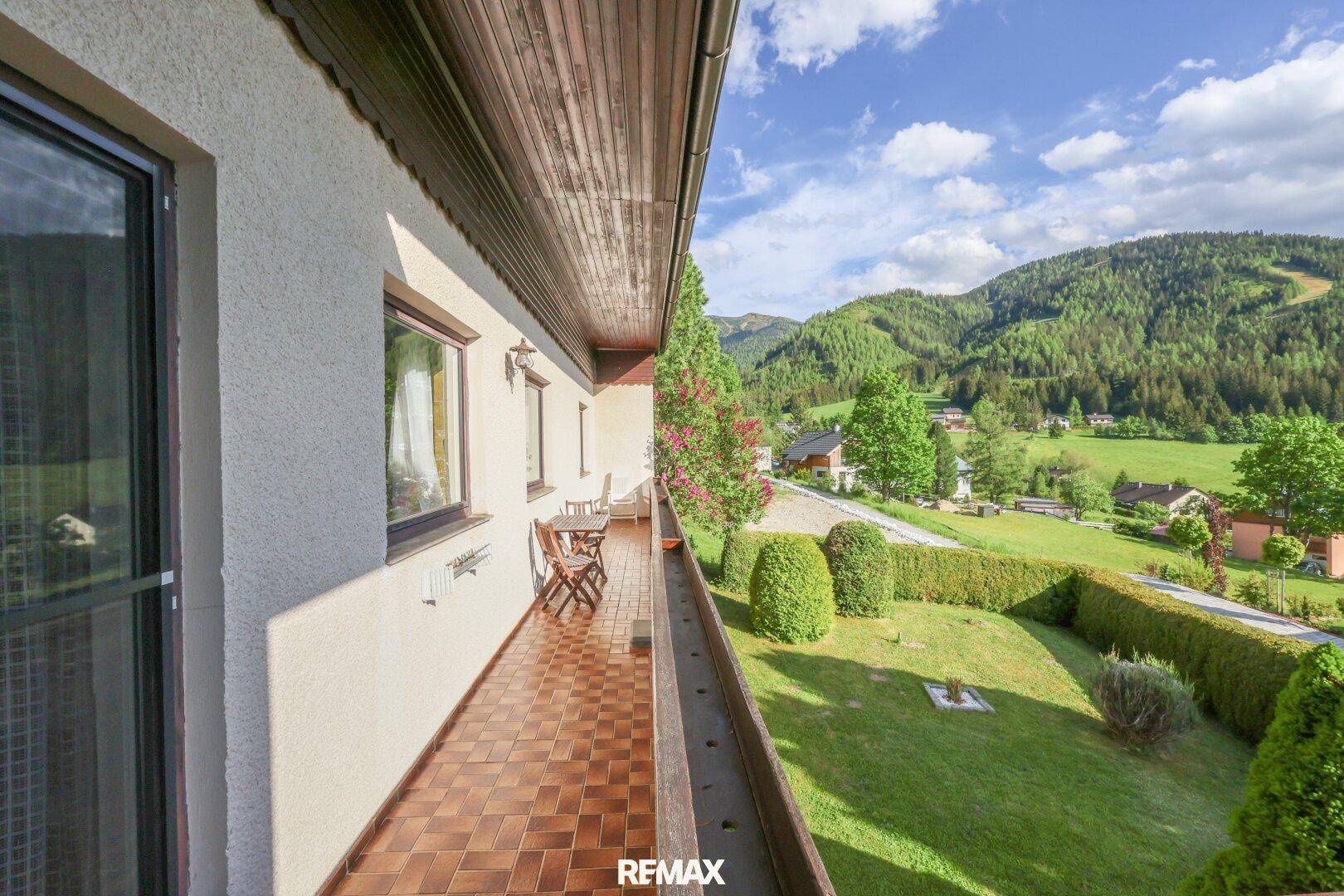 Langer Balkon mit Fliesenboden, Sitzgelegenheiten und weitem Blick auf die Berge und grüne Landschaft.