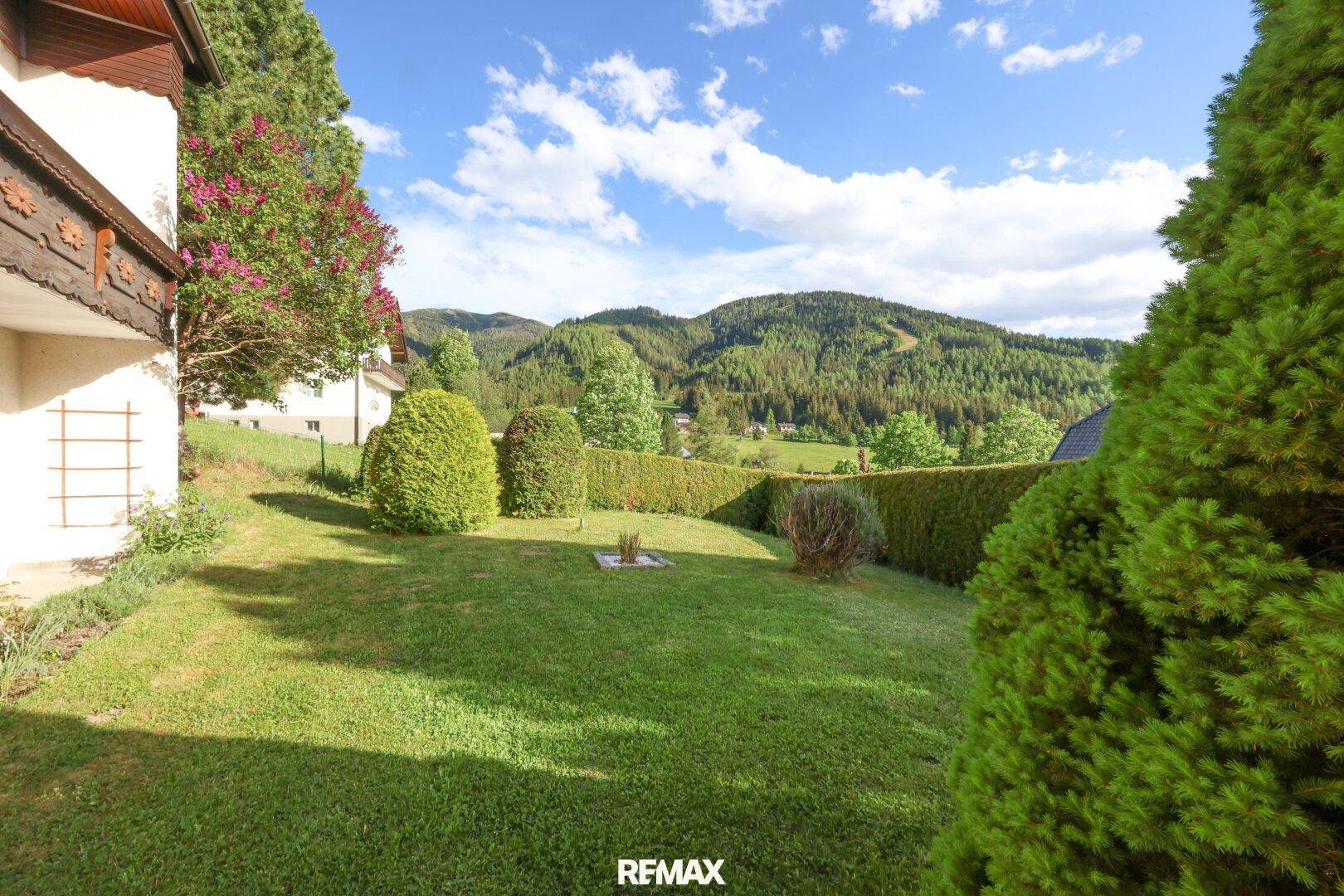 Gepflegter Gartenbereich mit Rasenfläche, Hecken und malerischem Bergblick.