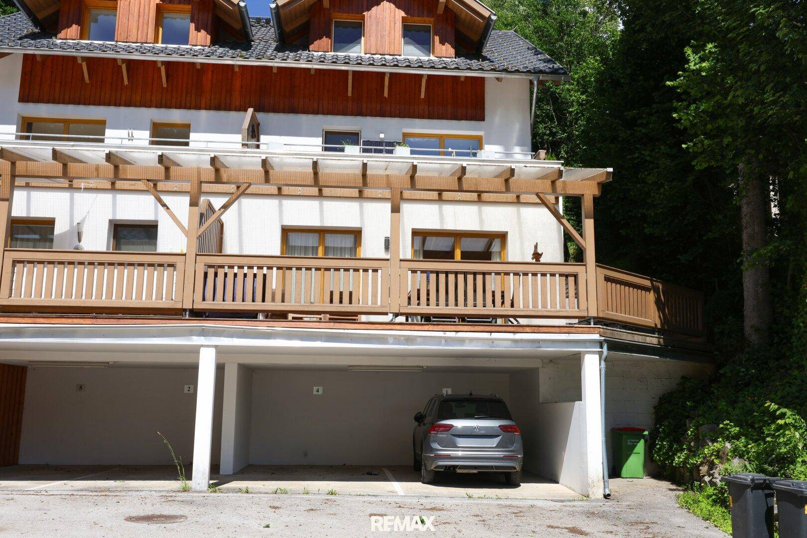 Ansicht des Gebäudes mit überdachten Parkplätzen und Holzterrassen in natürlicher Umgebung.