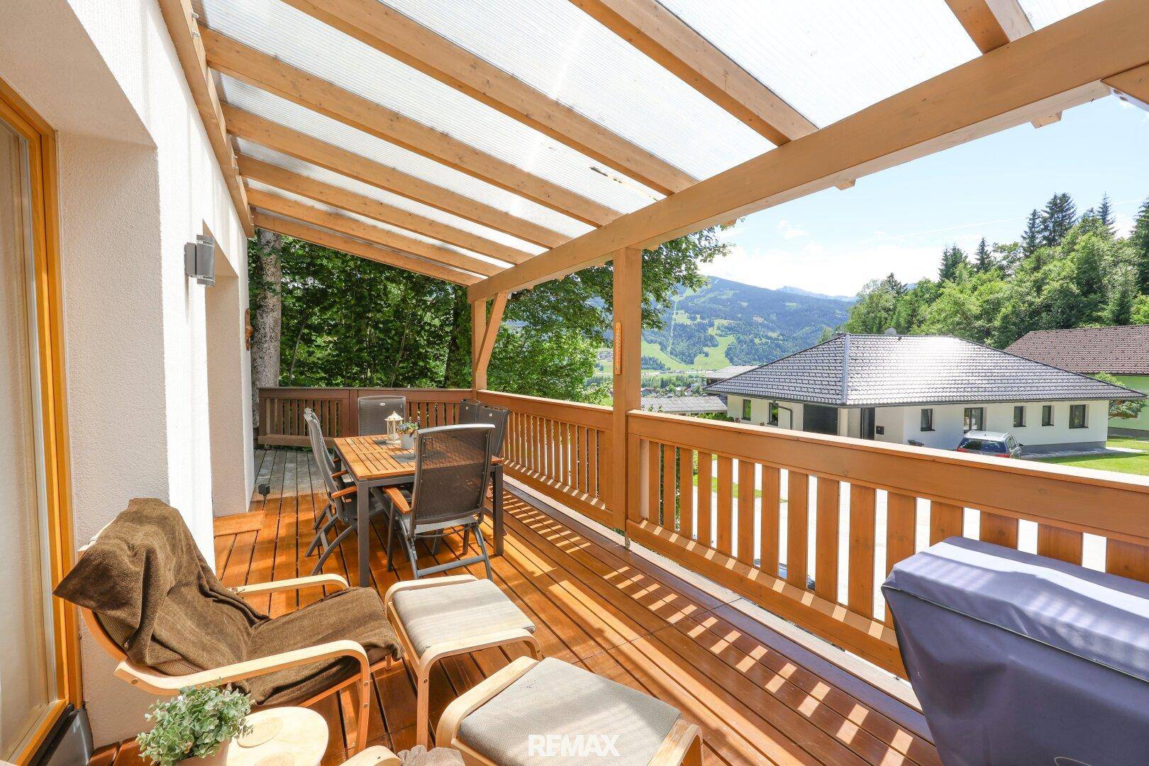 Geräumige überdachte Holzterrasse mit Esstisch und Lounge-Möbeln, umgeben von Natur.