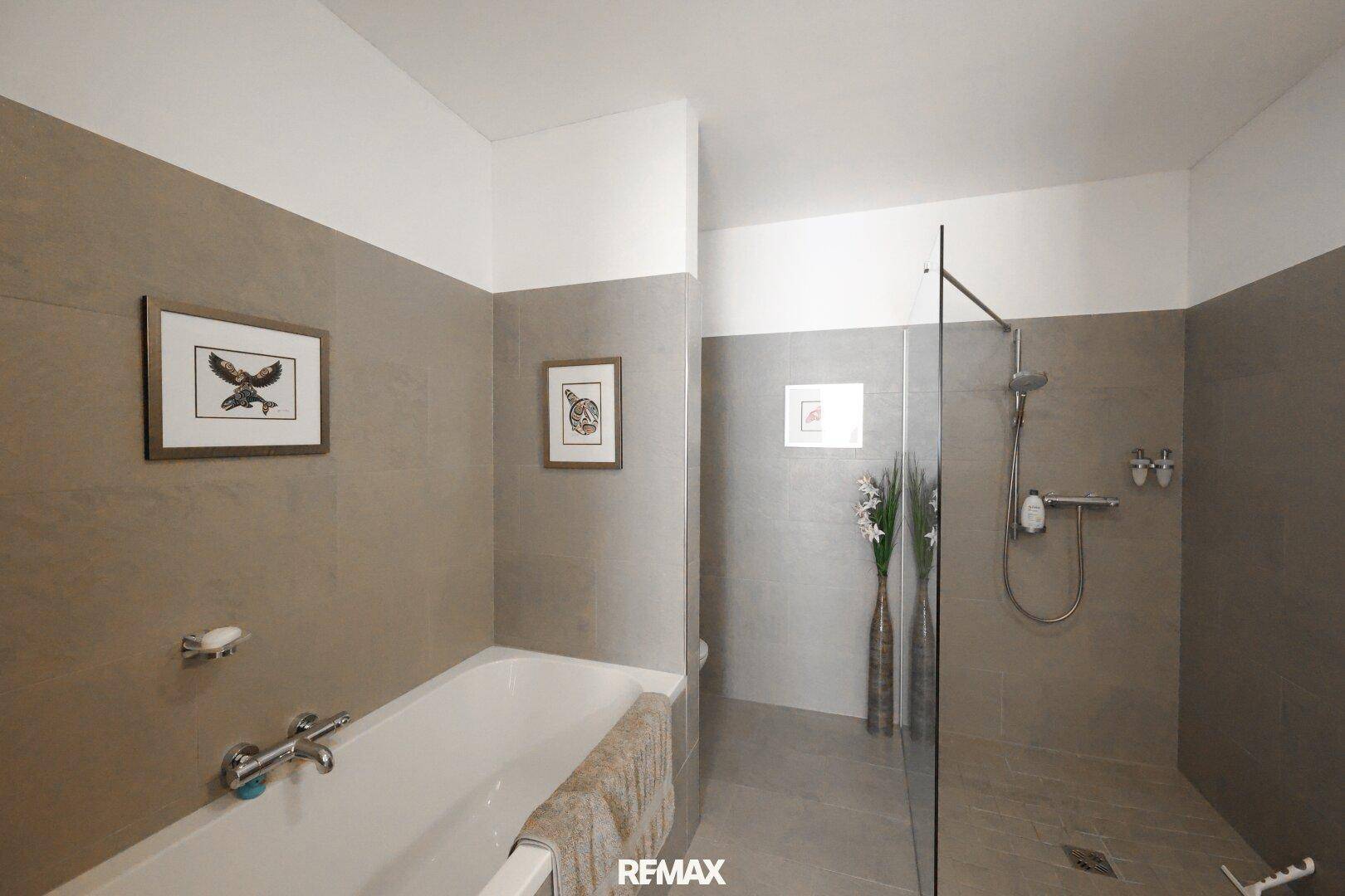 Modernes Badezimmer mit Badewanne, begehbarer Dusche und eleganten grauen Fliesen.