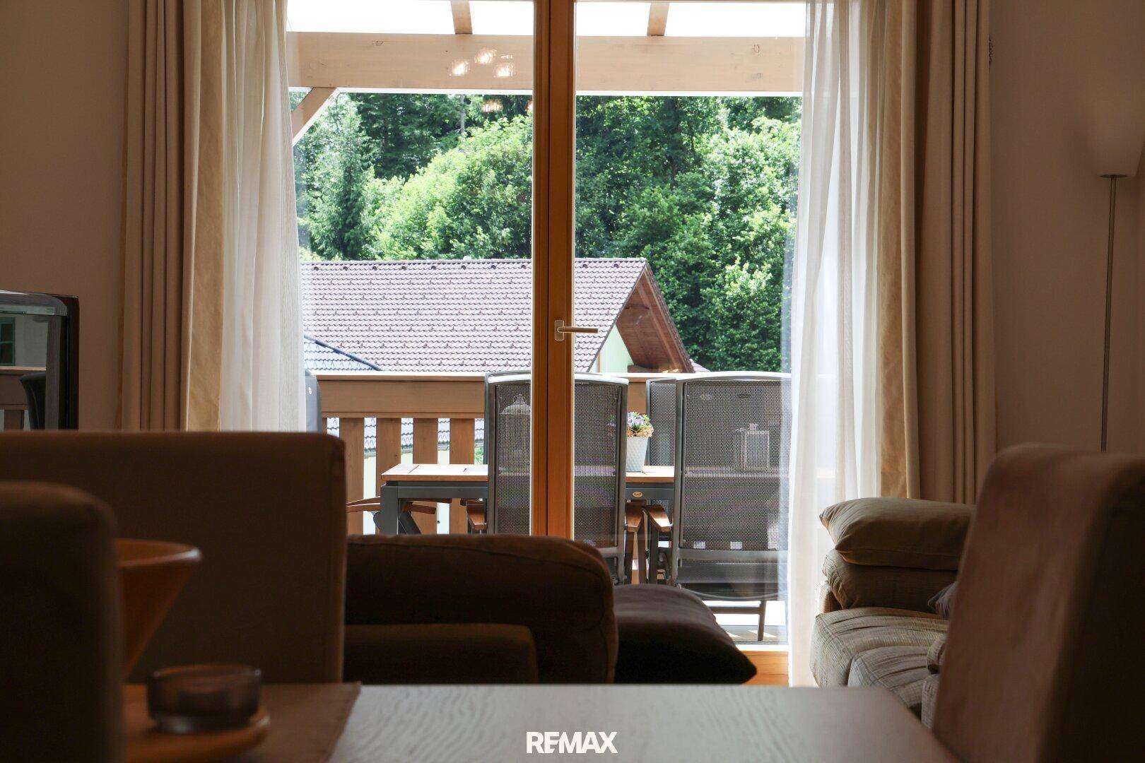 Blick vom Wohnzimmer auf die Terrasse mit Gartenmöbeln und grüner Umgebung.
