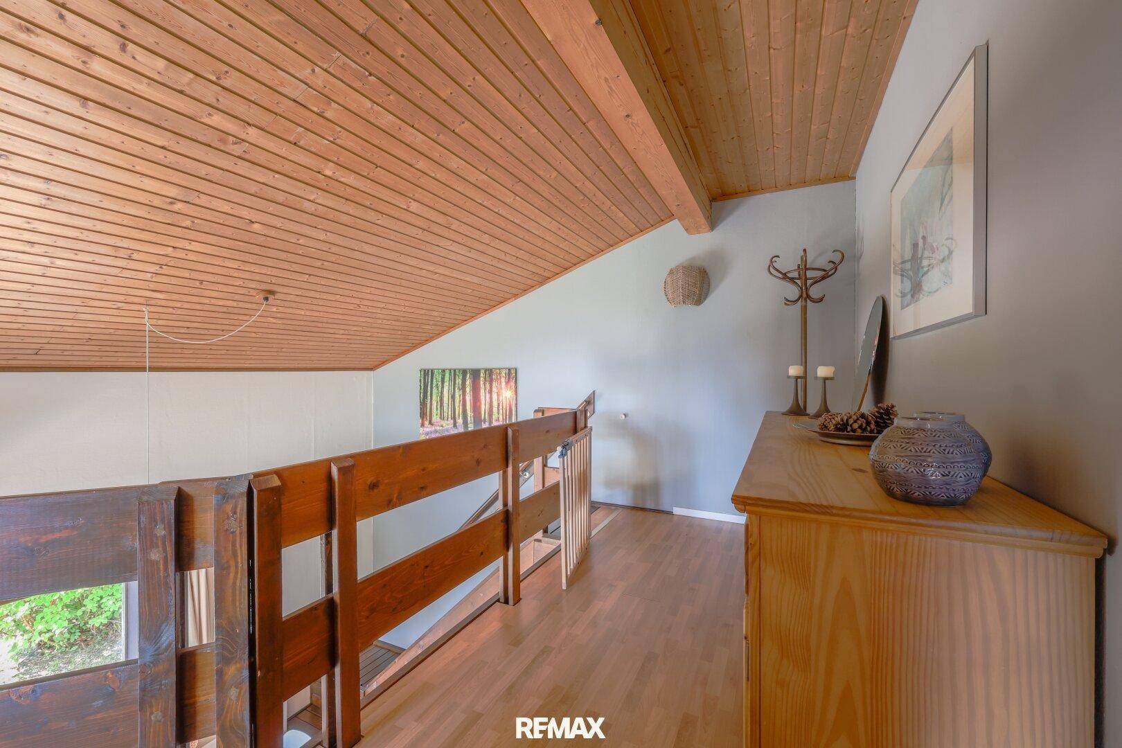 Heller Flur im Obergeschoss mit Holzgeländer und Holzdecke.