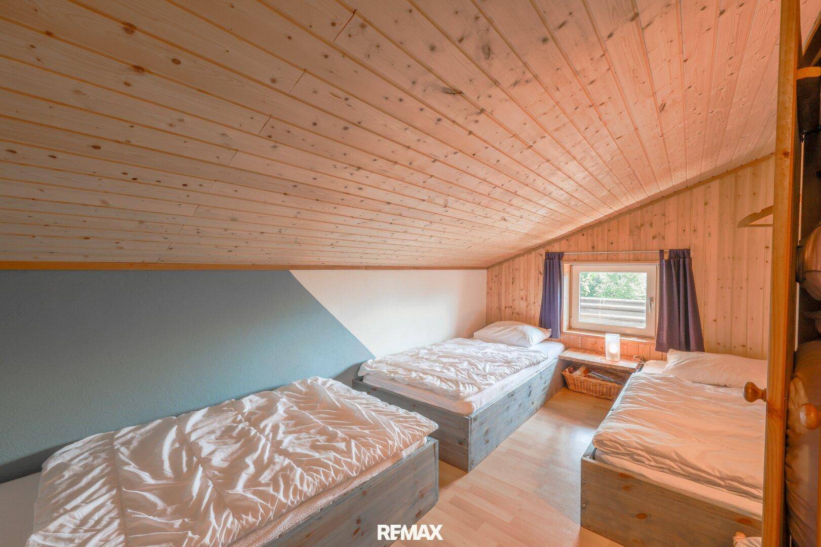 Schlafzimmer im Dachgeschoss mit drei Einzelbetten, Holzdecke und Dachschräge.