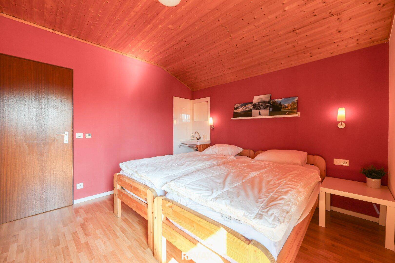 Schlafzimmer mit Doppelbett, rot gestrichener Wand und integriertem Waschbecken.
