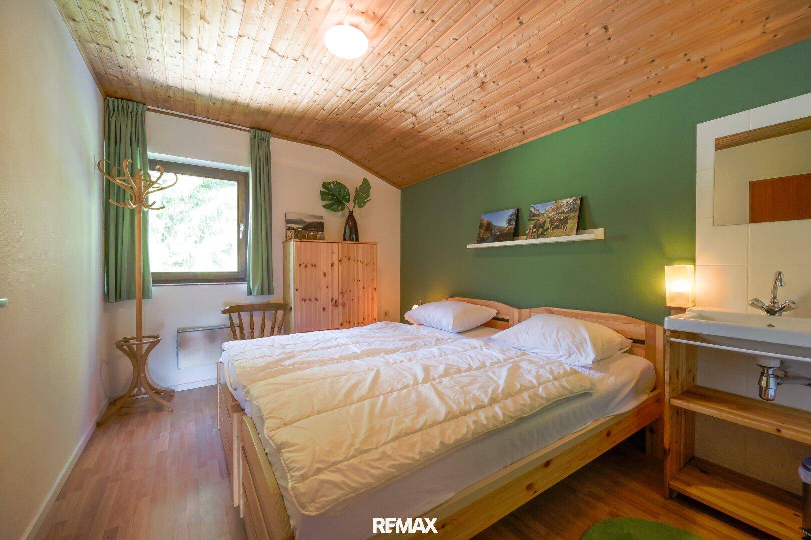 Schlafzimmer mit Doppelbett, grün gestrichener Wand und integriertem Waschbecken.