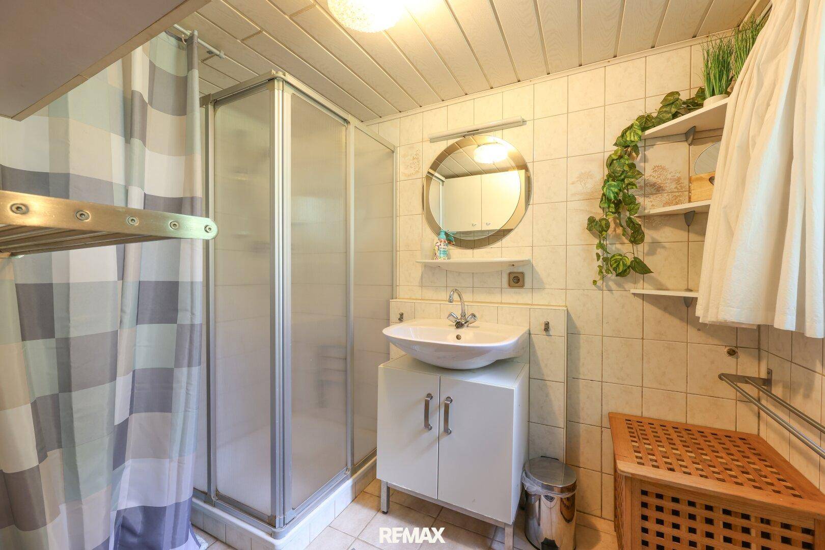 Badezimmer mit Duschkabine, Waschbecken und weißen Fliesen an Wänden und Boden.