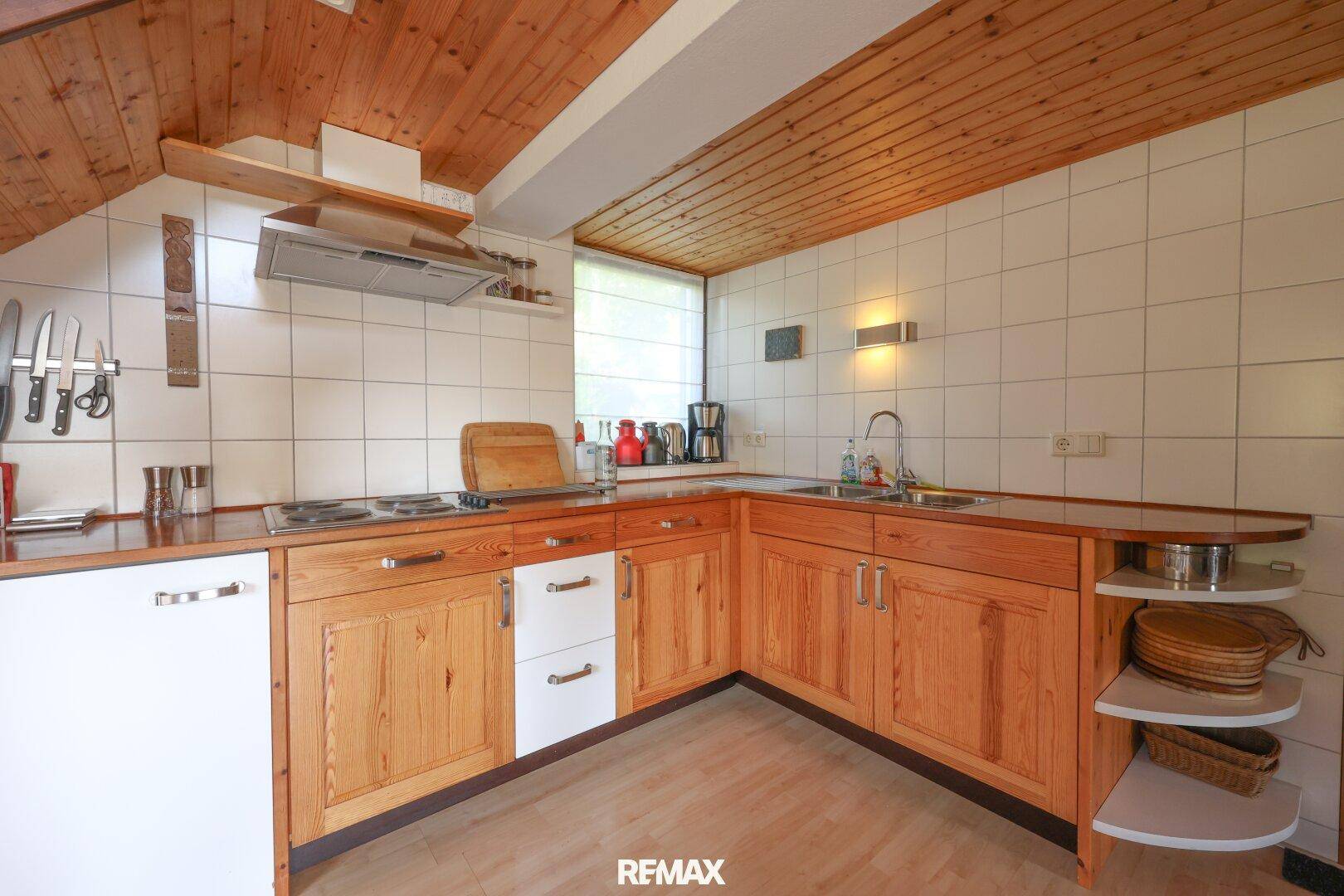 Funktionale Küche mit Holzschränken, weißen Fliesen und Dachschräge.