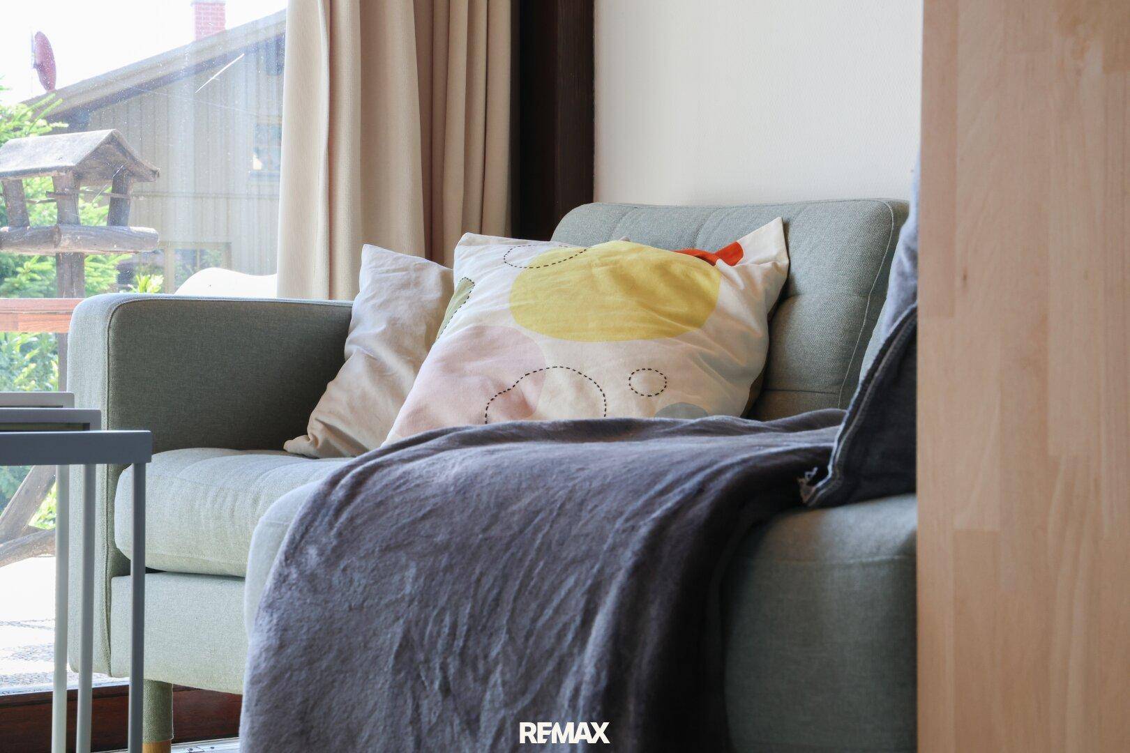 Detailaufnahme einer bequemen Couch mit bunten Kissen und weicher Decke im Wohnzimmer.