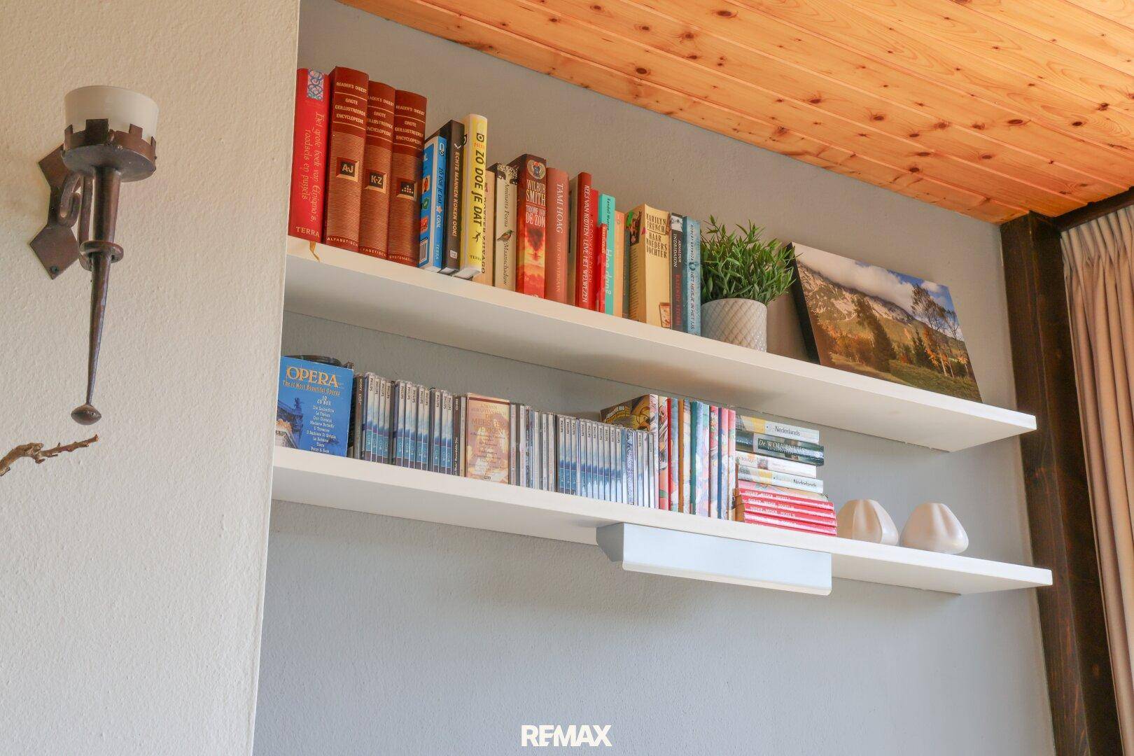 Bücherregale mit Büchern und Dekoration an einer Wand, unter einer Holzdecke.