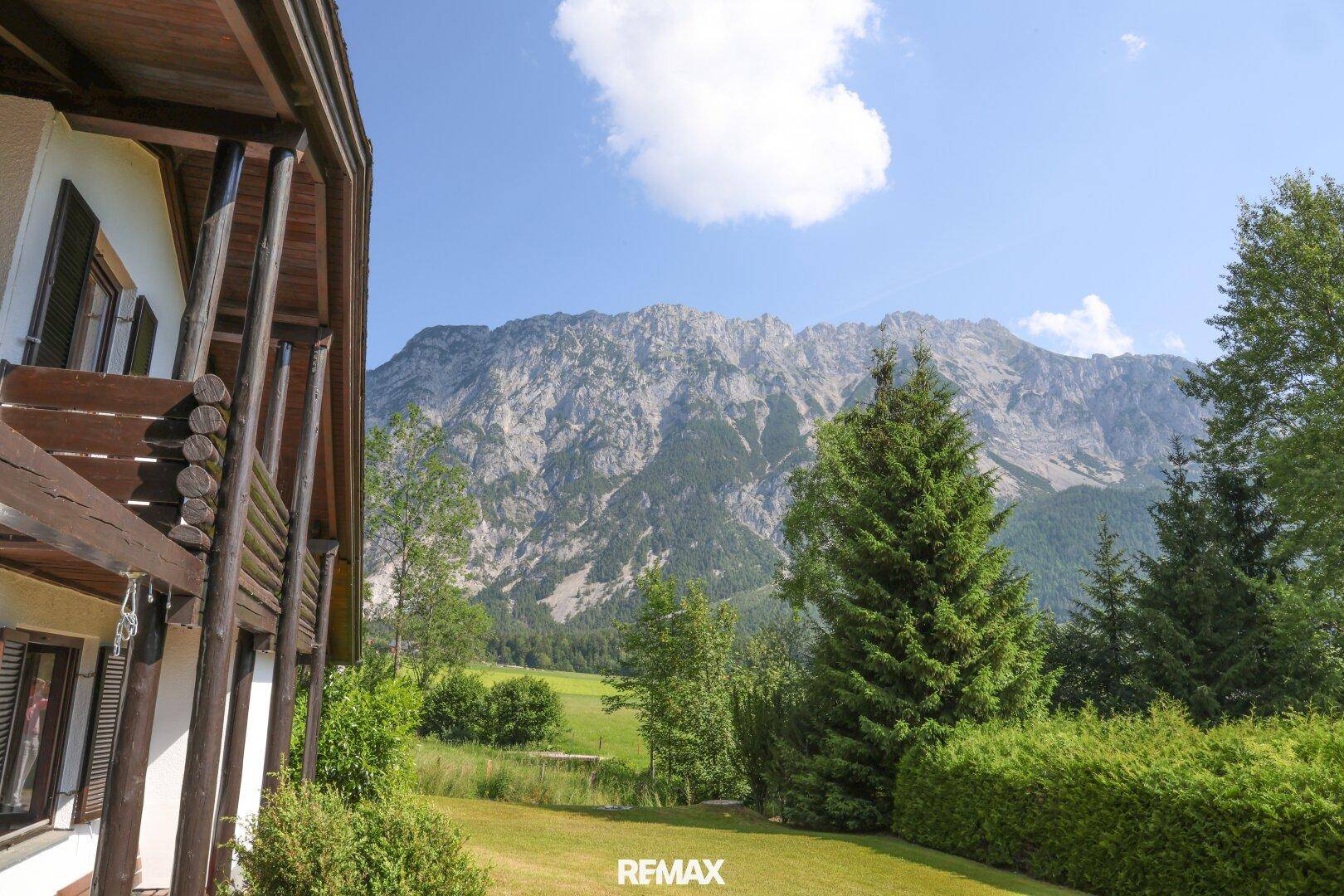 Ansicht des Hauses mit Holzbalkon und beeindruckendem Bergblick unter blauem Himmel.