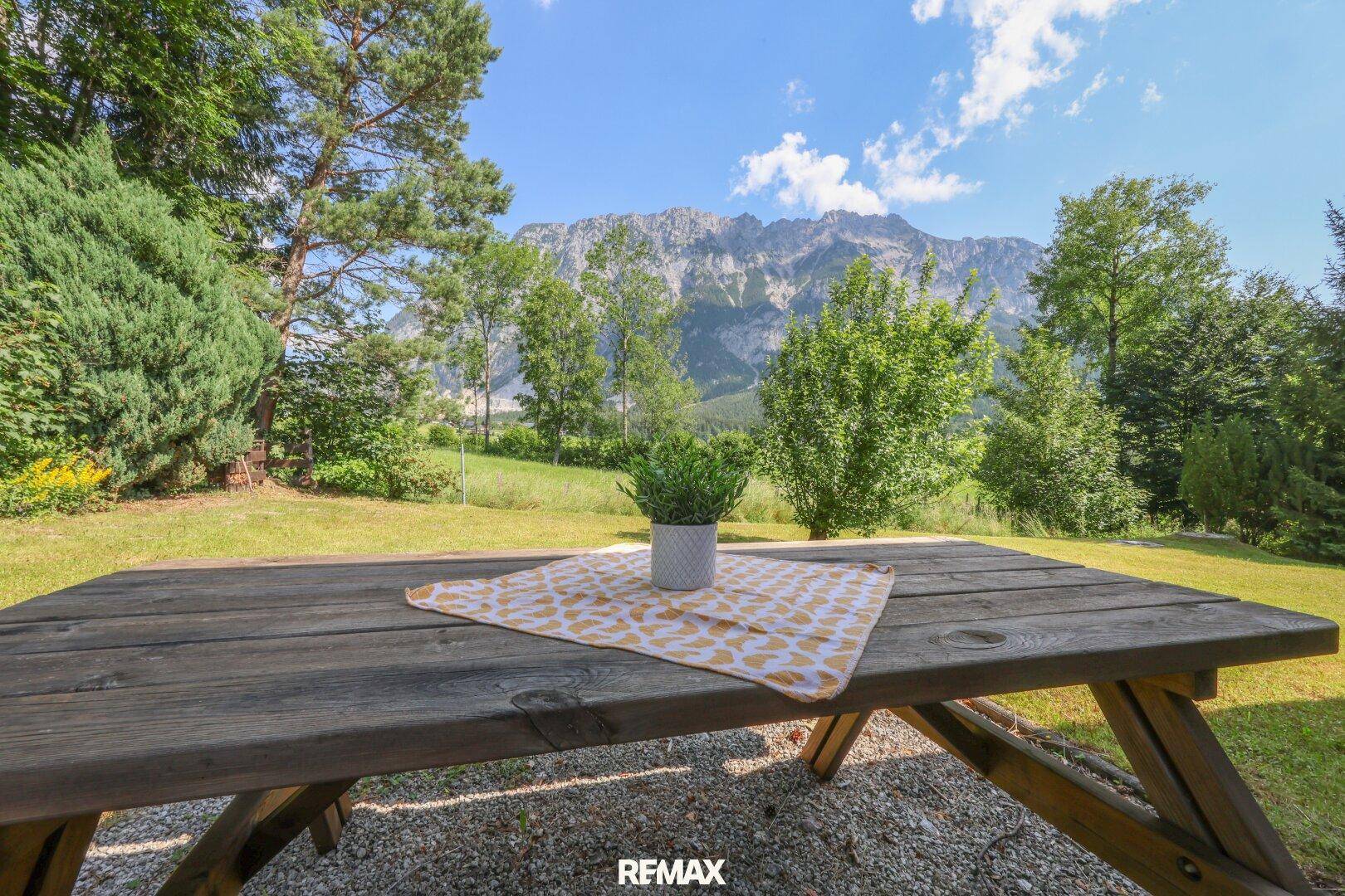 Rustikaler Picknicktisch im Garten mit Blick auf die Berge und die grüne Landschaft.