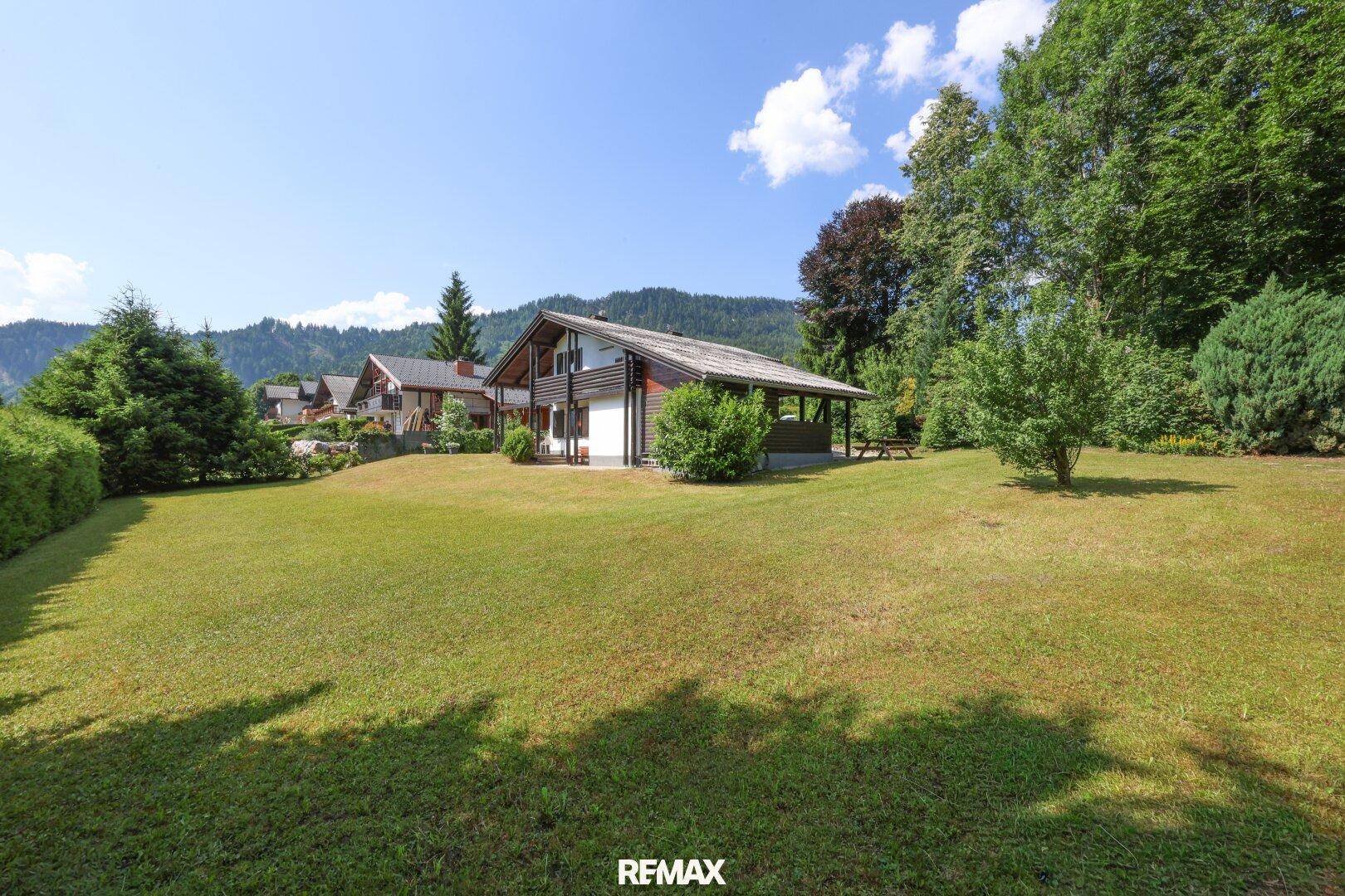 Weitläufiger grüner Garten mit Blick auf das Haus und die bewaldeten Berge im Hintergrund.