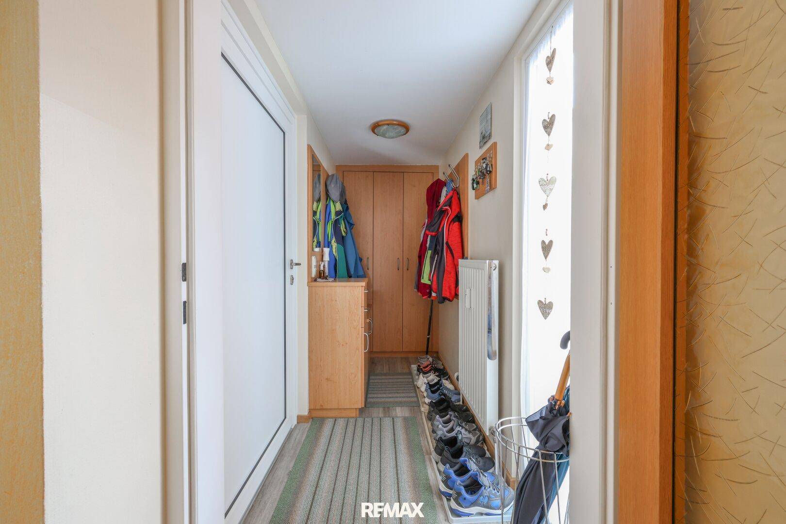 Heller Flur mit Garderobe, Schuhregal und Holzelementen, der zum Wohnbereich führt.