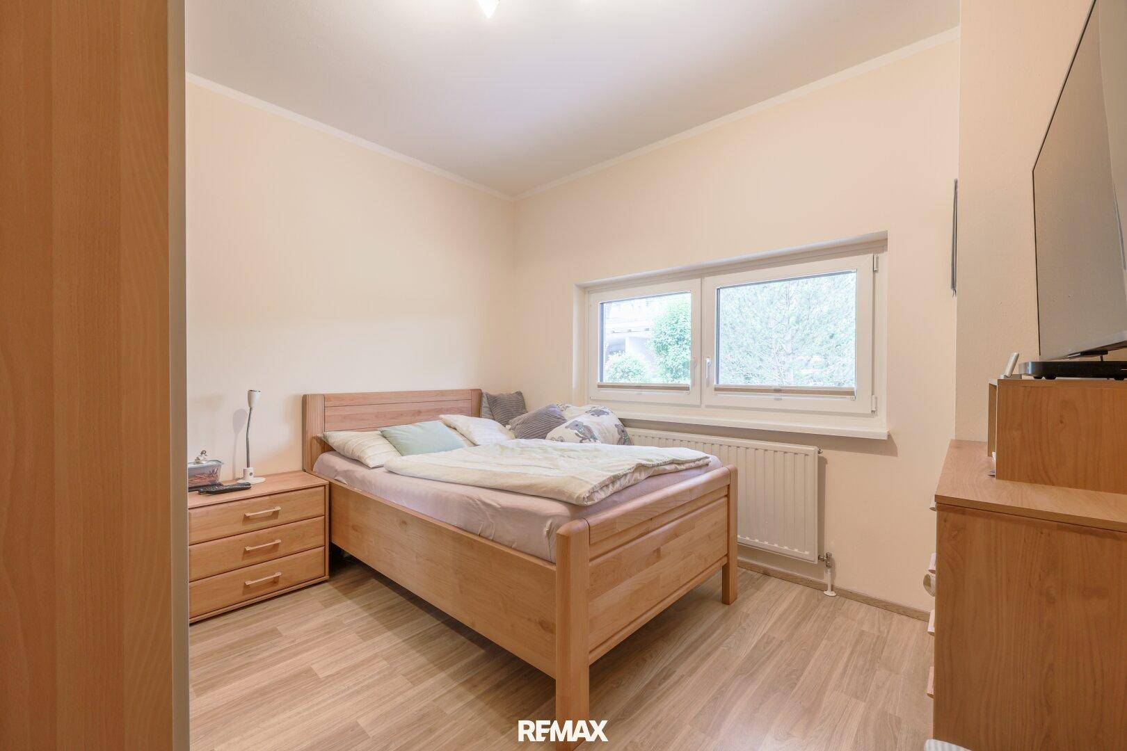 Gemütliches Schlafzimmer mit Holzbett, Nachttischen und Laminatboden, hell durch ein Fenster.