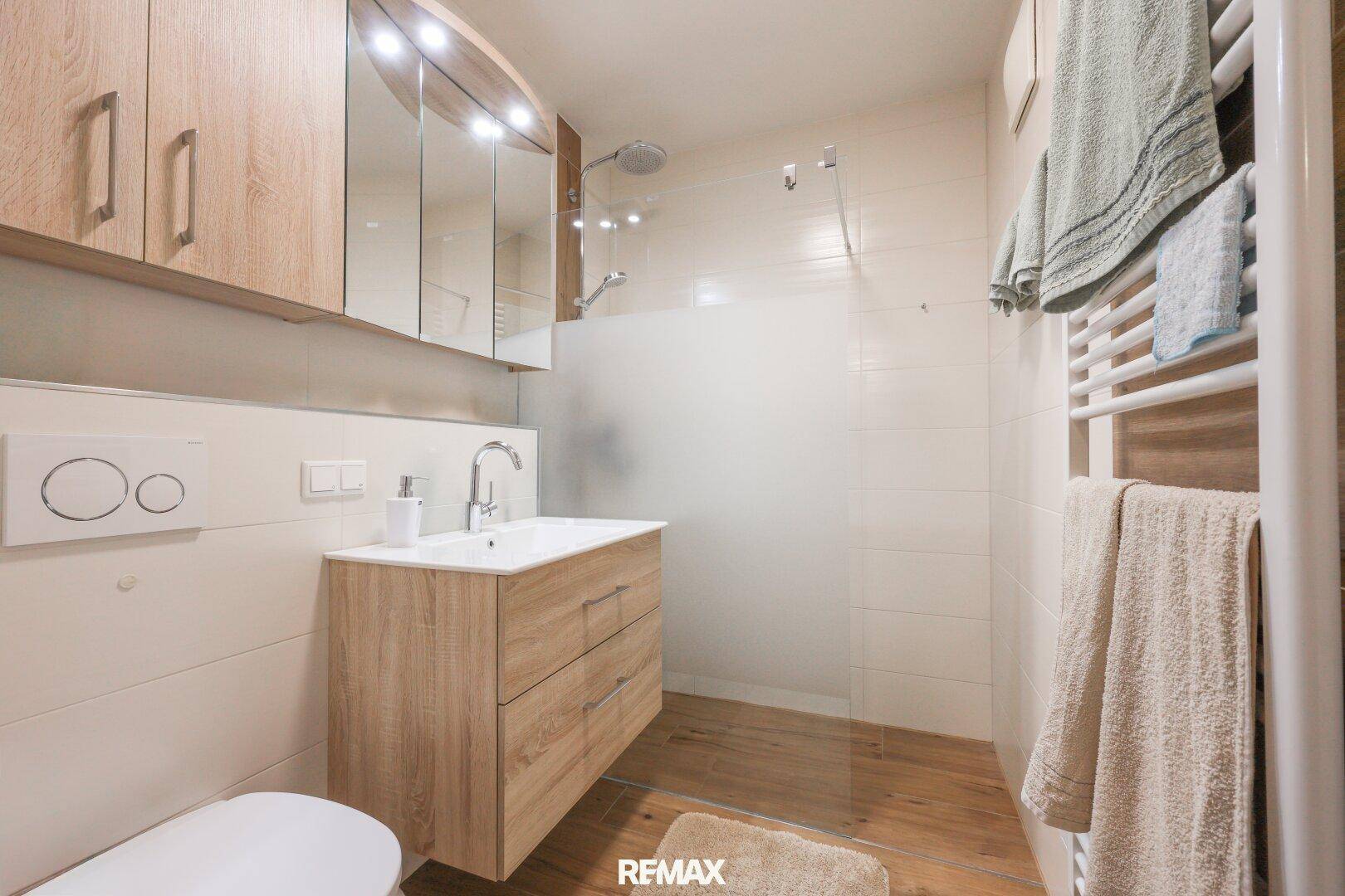 Modernes Badezimmer mit Holzelementen, Einzelwaschbecken, Dusche und beheiztem Handtuchhalter.