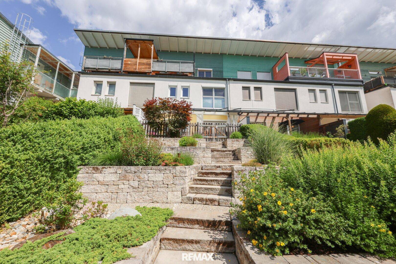 Mehrere Reihenhäuser mit Terrassen und einem terrassierten Gartenbereich mit Steinstufen.